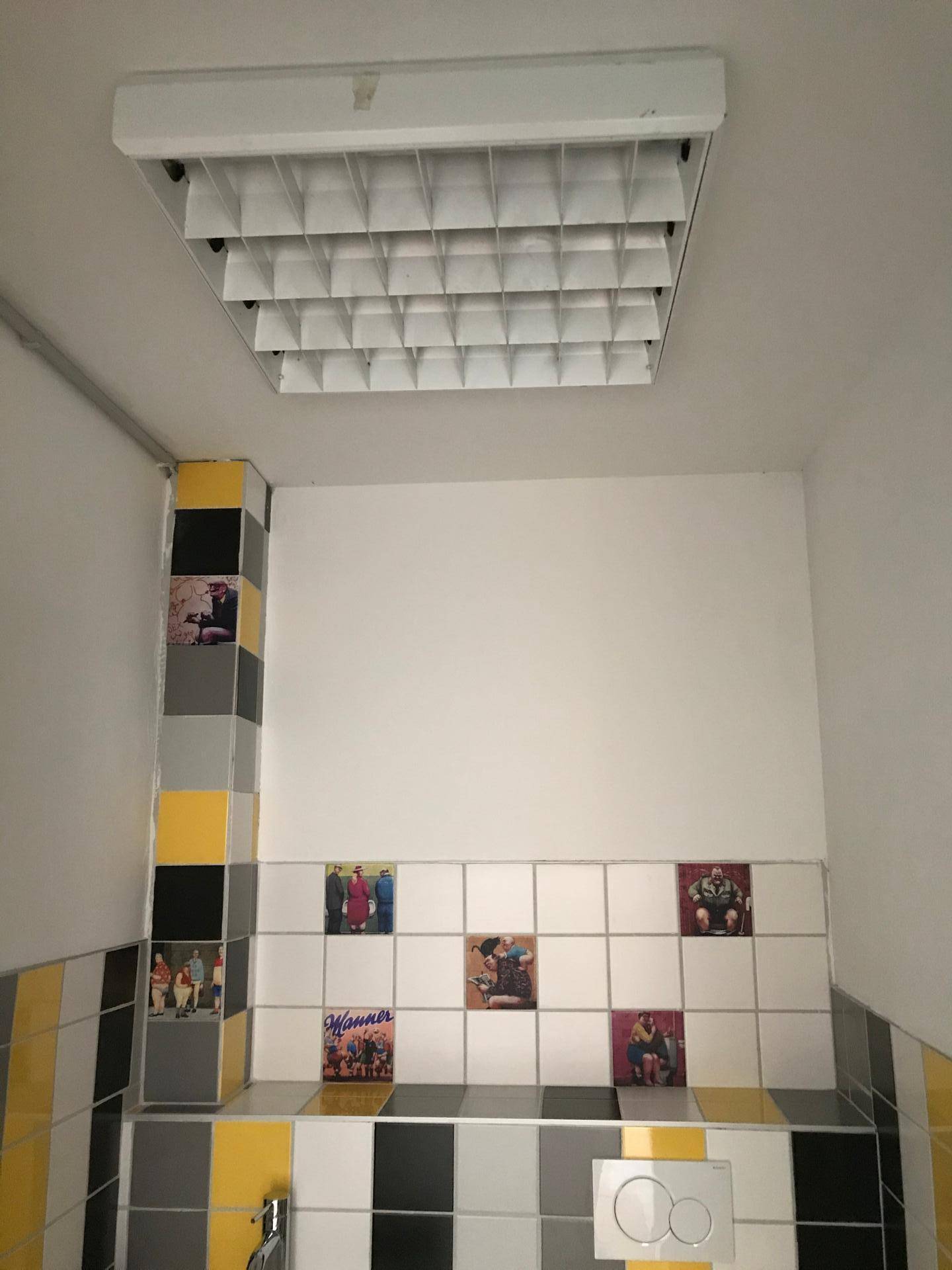 Buntes Gäste-WC mit gelben, schwarzen und grauen Fliesen sowie Deckenleuchte.