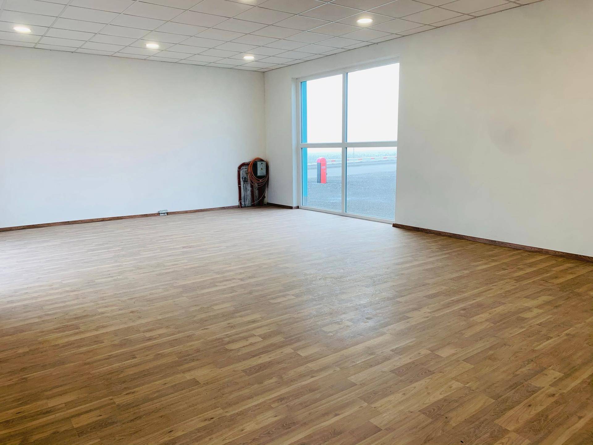 Geräumiger, heller Raum mit Laminatboden, großen Fenstern und einer modernen Deckenbeleuchtung.