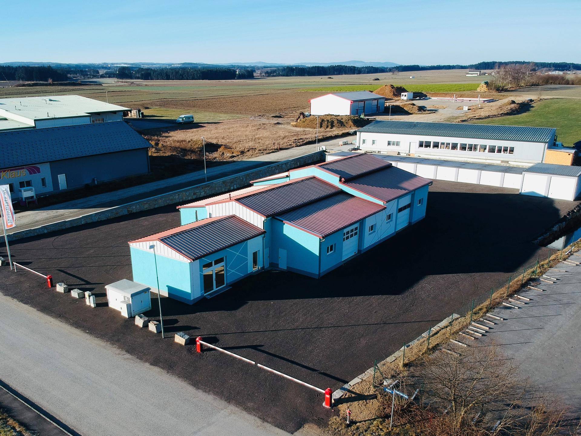 Drohnenansicht des Gewerbeobjekts mit blauer Fassade, rotem Dach und umliegenden Feldern.