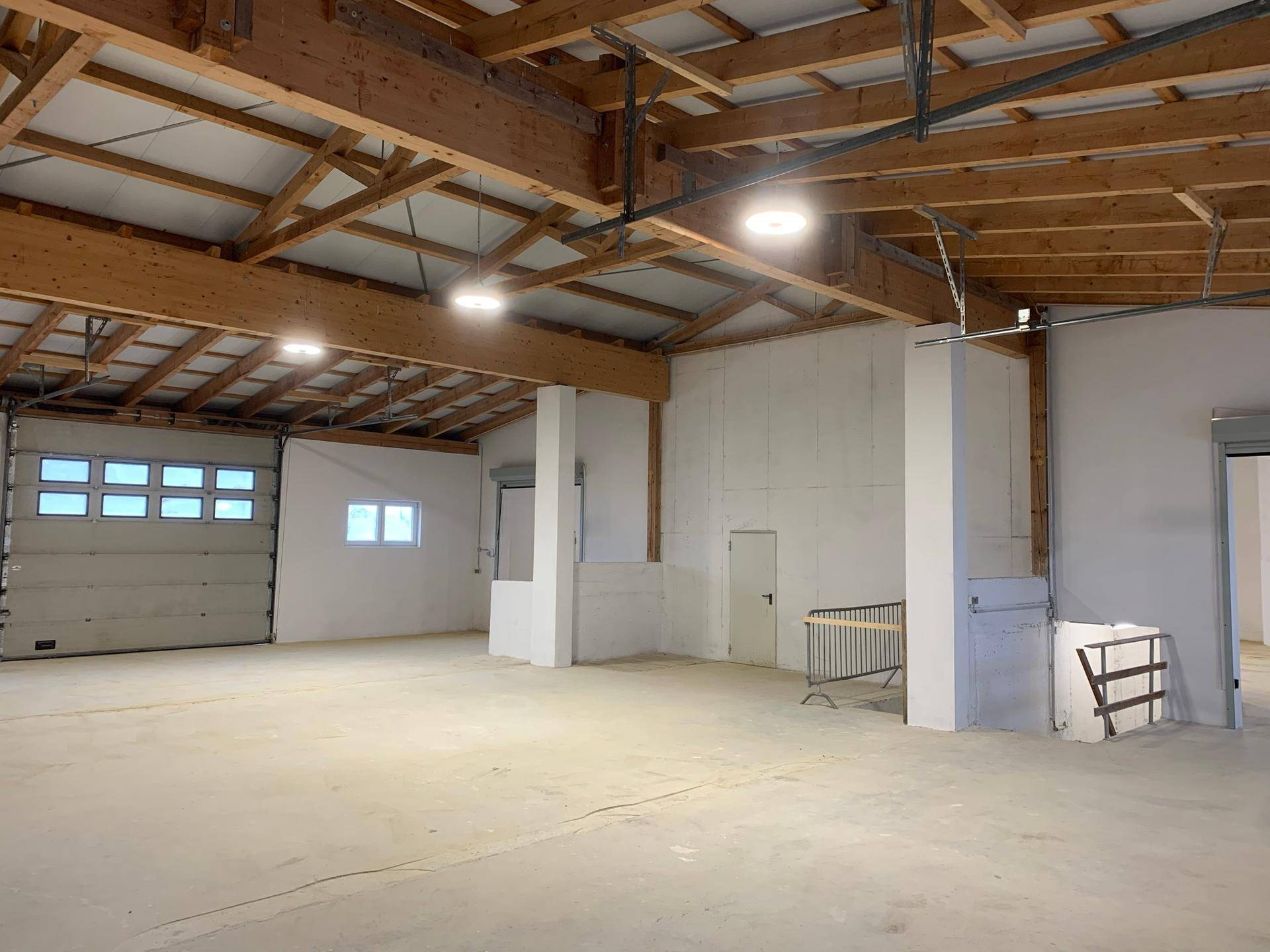 Große Lagerhalle mit hohen Decken, sichtbaren Holzbalken und einem Rolltor.