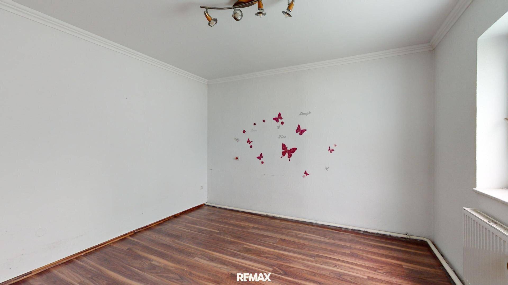 Leeres Zimmer mit weißen Wänden, einem Fenster und Laminatboden, verziert mit Schmetterlingsaufklebern.