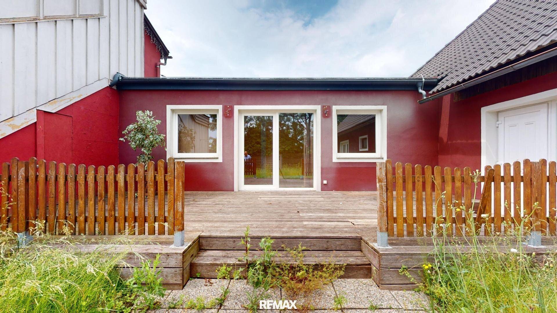 Hinterer Bereich des Gebäudes mit einer Holzterrasse, einem Holzzaun und großen Glasschiebetüren.