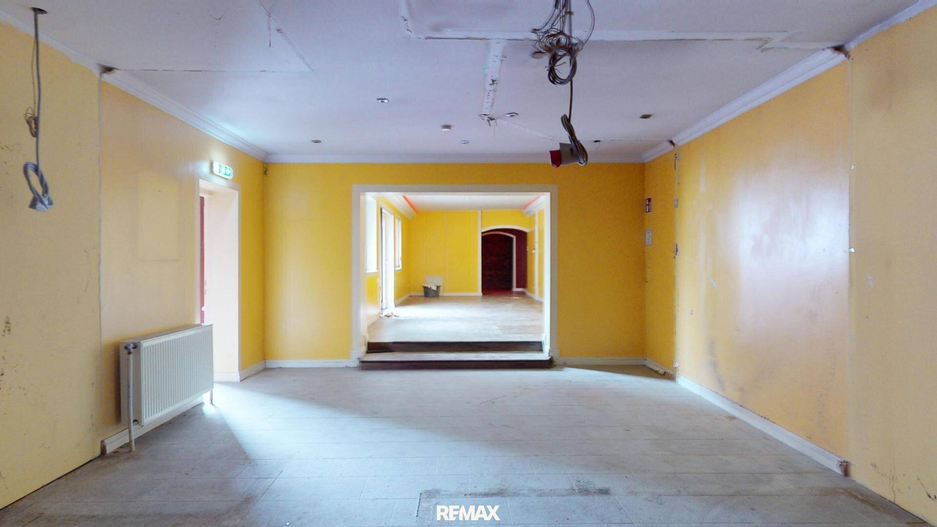 Leerer Raum mit gelben Wänden, einem Heizkörper und einem Durchgang zu einem weiteren Zimmer.