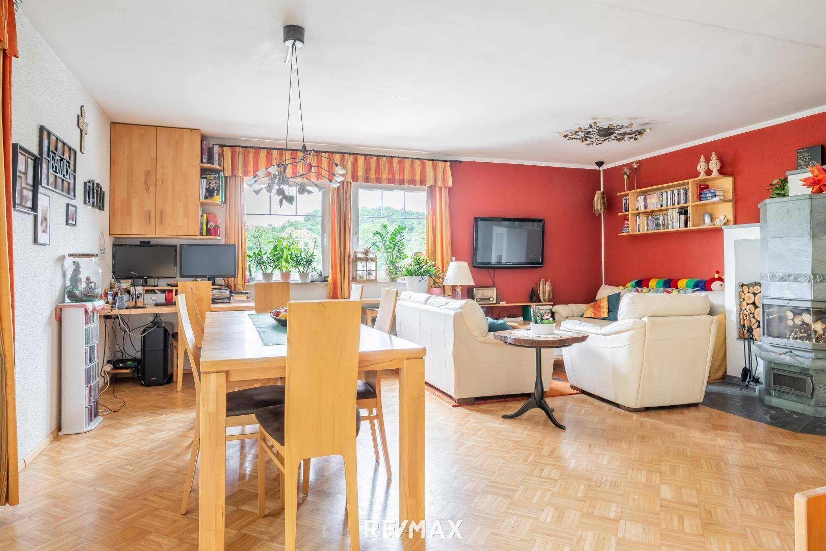 Geräumiger Wohn-Essbereich mit Parkettboden, Kaminofen und Blick ins Grüne durch große Fenster.