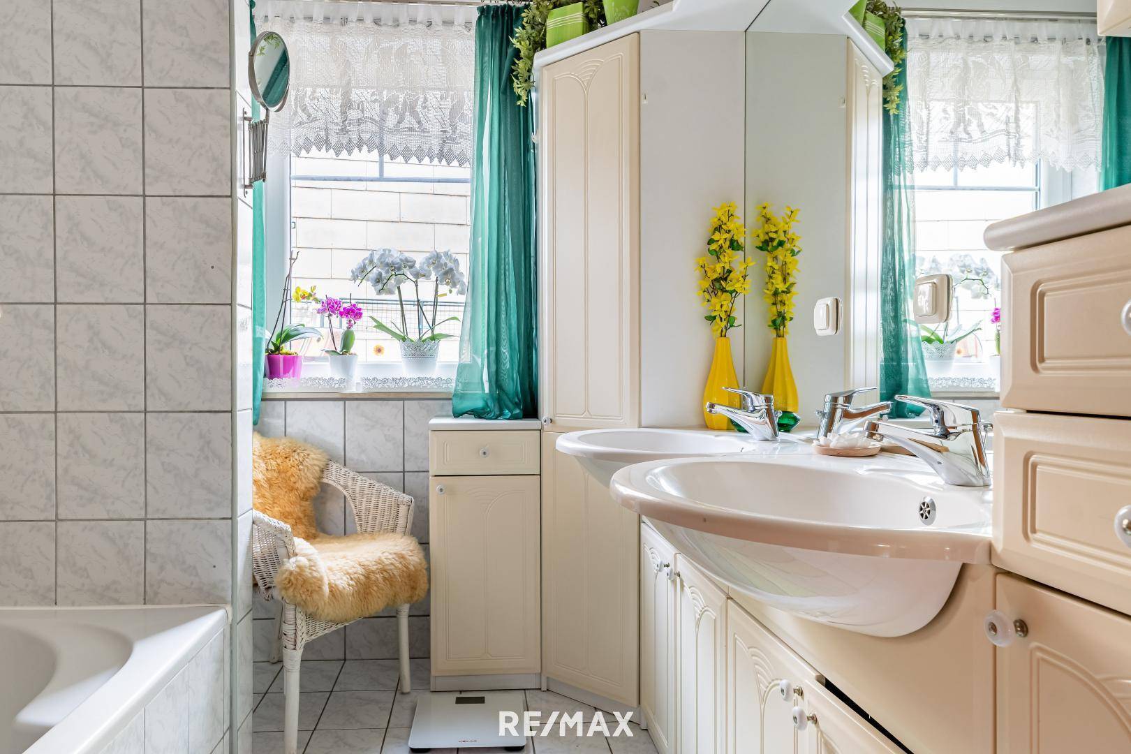 Helles Badezimmer mit Doppelwaschbecken, Badewanne und Fenster, dekoriert mit gelben Akzenten.