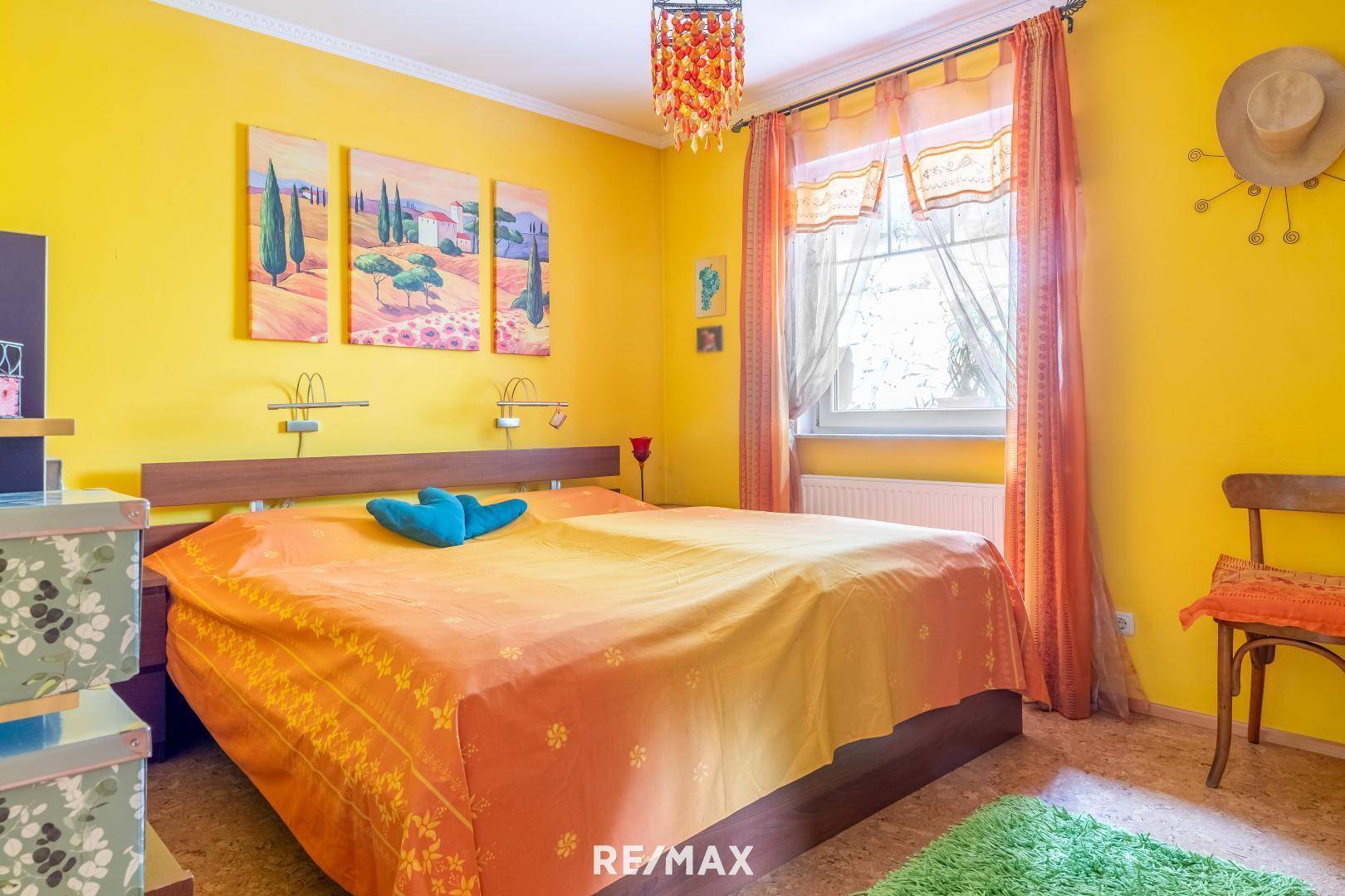 Farbenfrohes Schlafzimmer mit Doppelbett, gelben Wänden und Blick ins Grüne durch das Fenster.