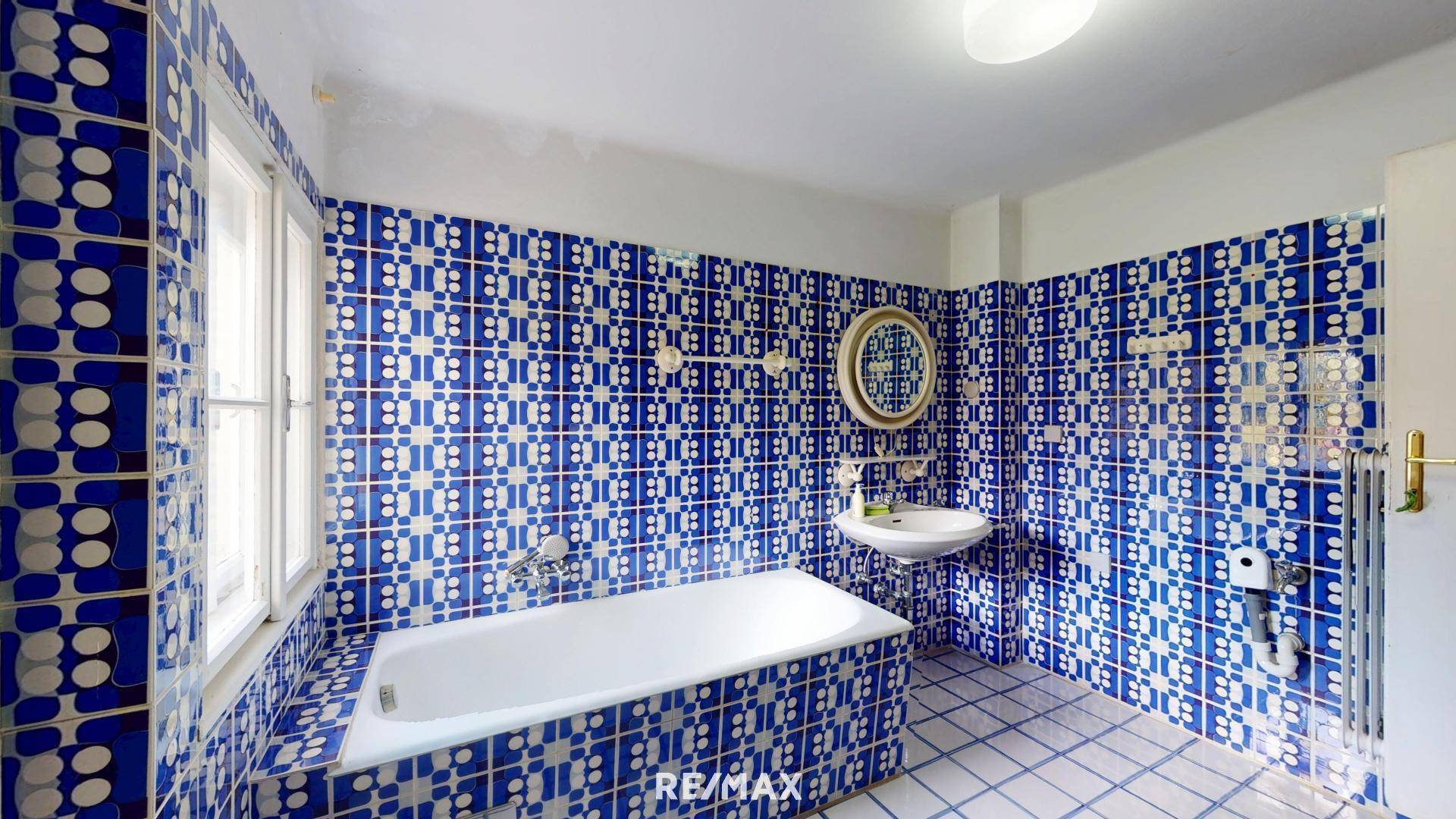 Badezimmer mit blauen, gemusterten Fliesen, Badewanne und Fenster.
