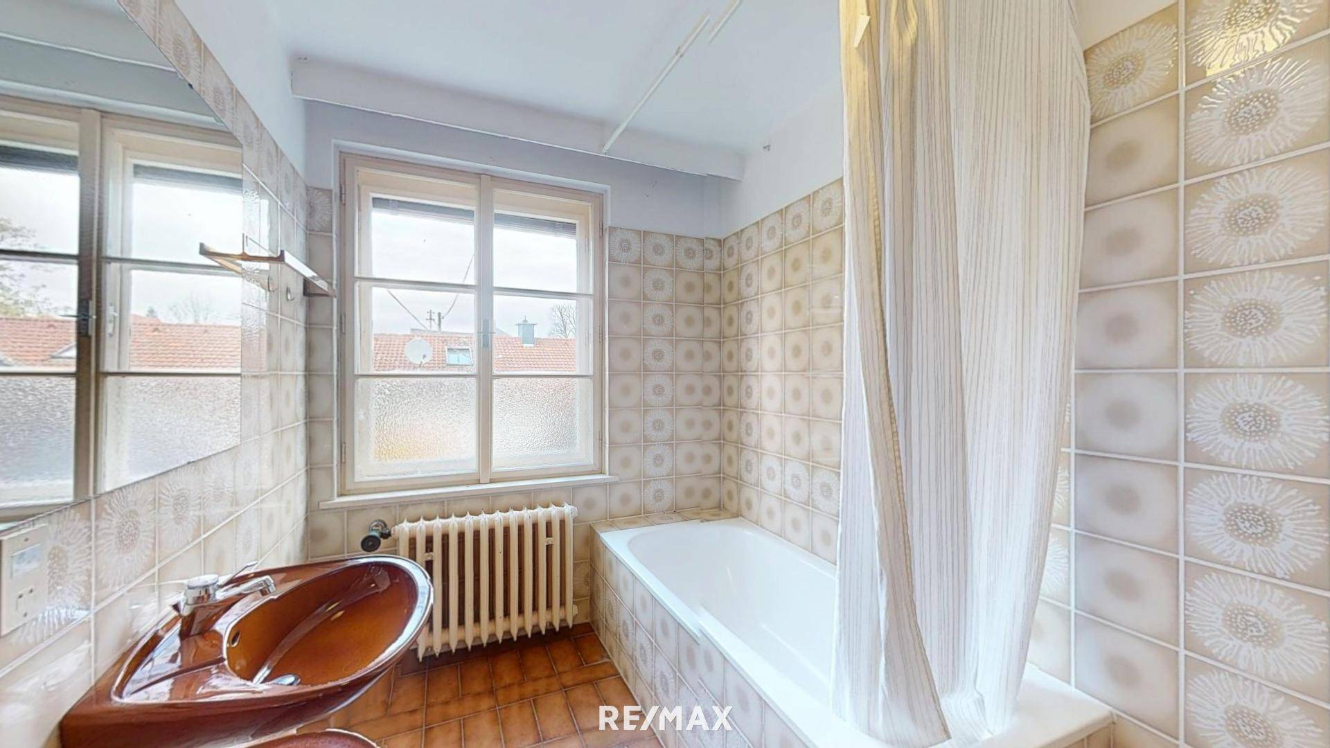 Badezimmer mit Badewanne, Fenster und gemusterten Fliesen im 80er-Jahre-Stil.