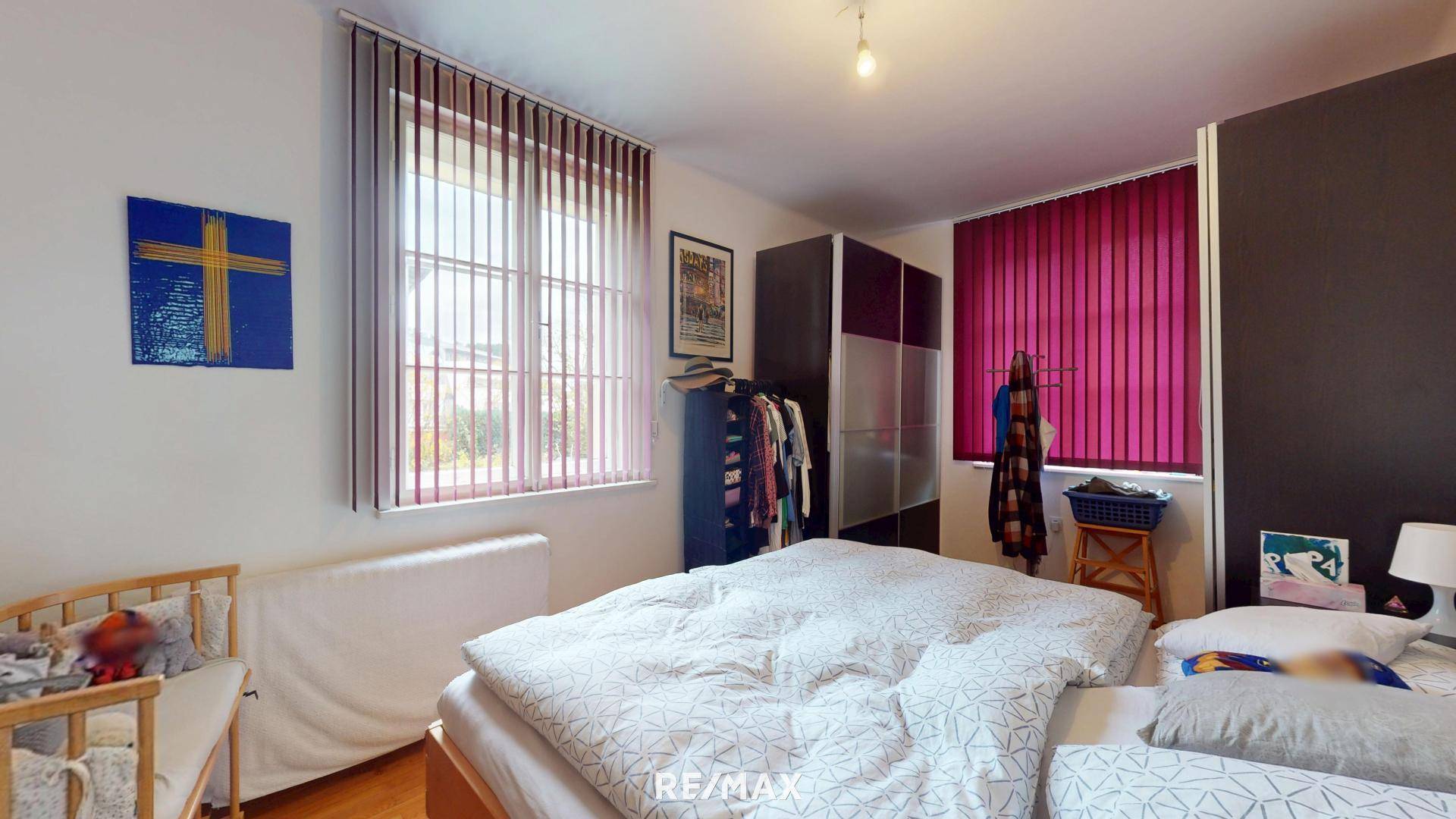 Schlafzimmer mit Doppelbett, Kleiderschrank und Fenster mit Jalousien.