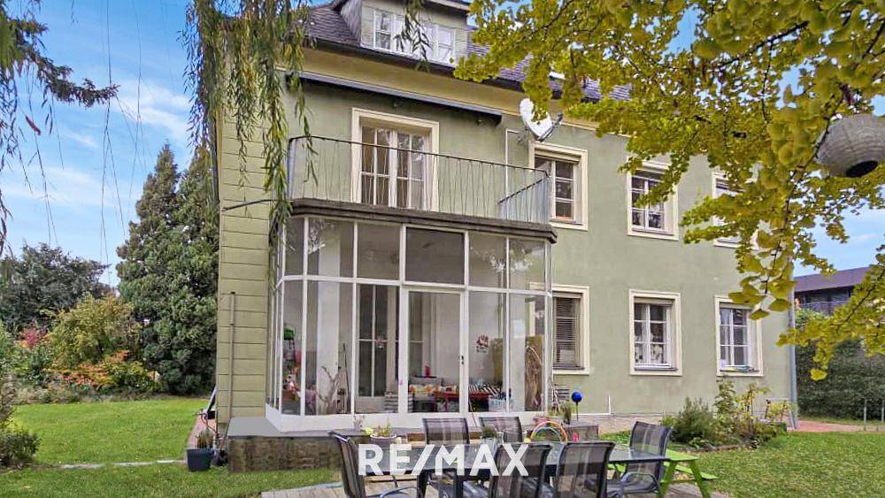 Rückseite des Hauses mit Wintergarten, möblierter Terrasse und großem Gartenbereich.