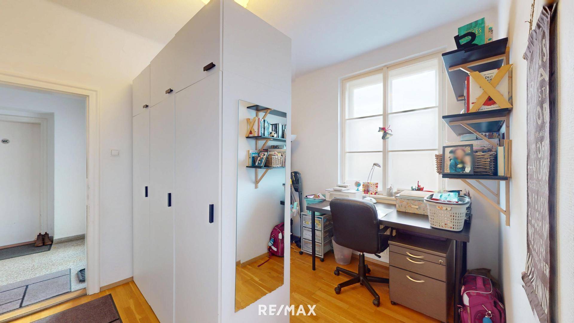 Helles Arbeitszimmer mit großem Kleiderschrank, Schreibtisch und Fenster.