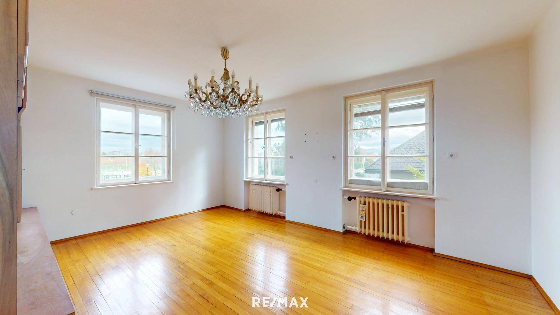 Helles, leeres Zimmer mit Parkettboden und großen Fenstern.