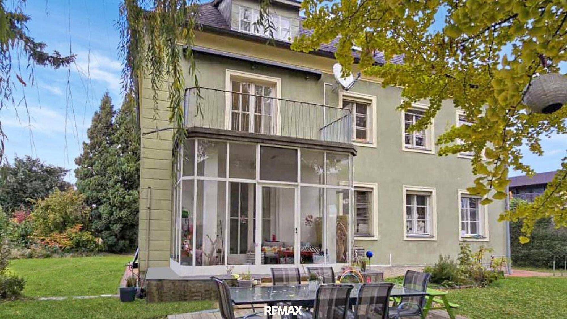 Rückseite des Hauses mit Wintergarten, Balkon und möblierter Terrasse im grünen Garten.
