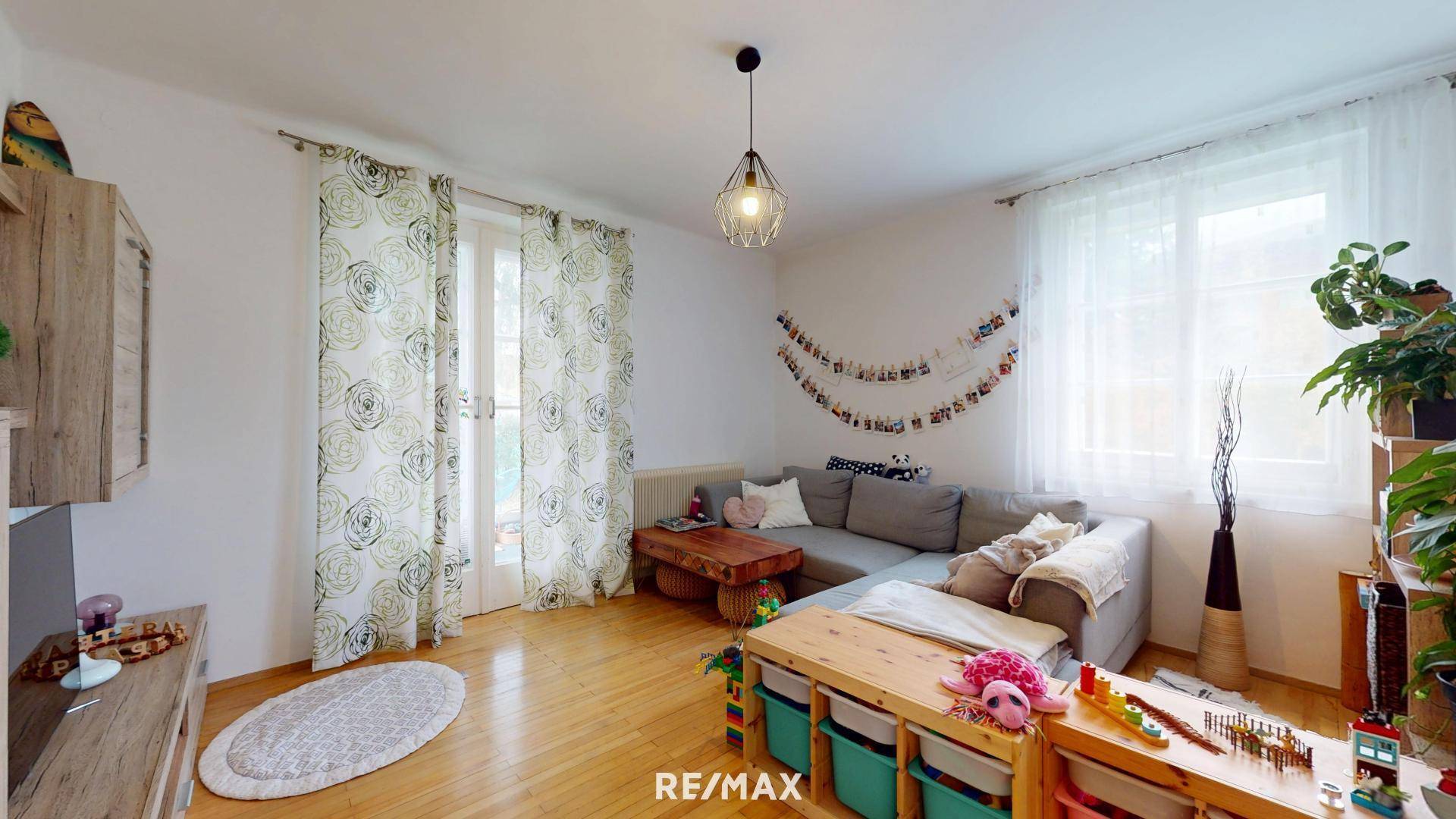 Gemütliches Wohnzimmer mit großem Sofa, Holzboden und Zugang zum Balkon.