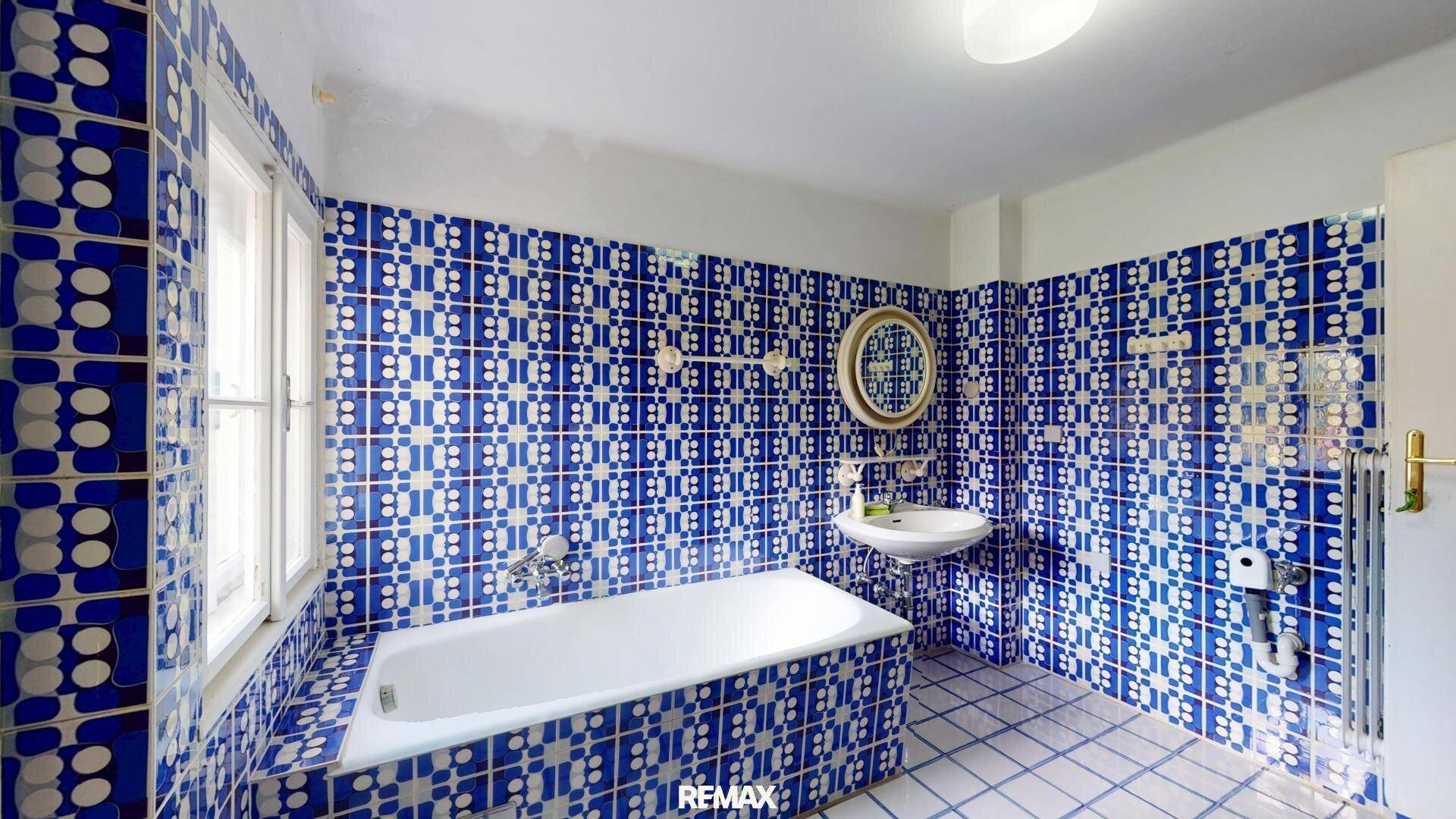 Badezimmer mit auffälligen blauen Fliesen, Badewanne und Fenster.