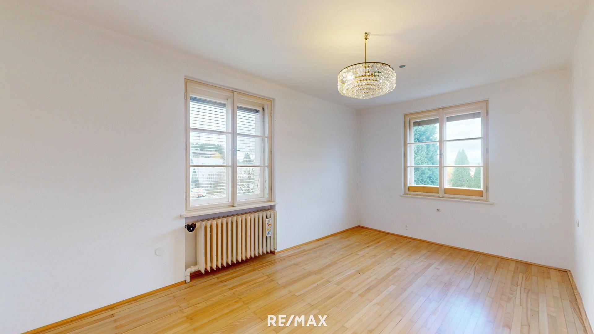 Leeres Zimmer mit Holzboden und zwei Fenstern.