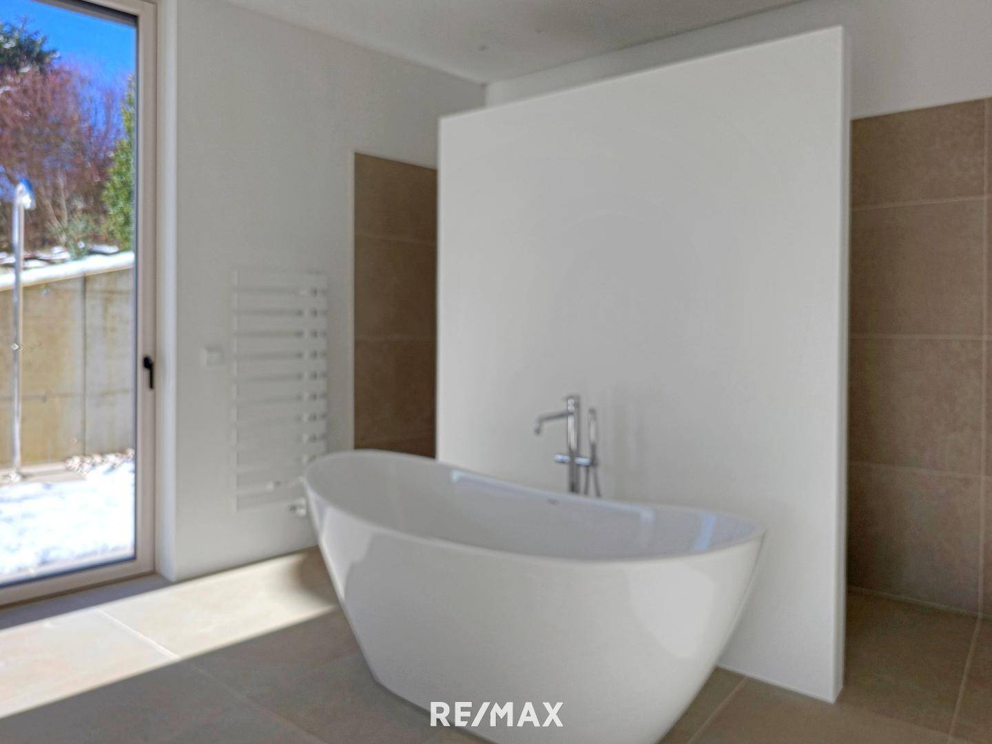 Modernes Badezimmer mit freistehender Badewanne und Fenster, das Tageslicht hereinlässt.