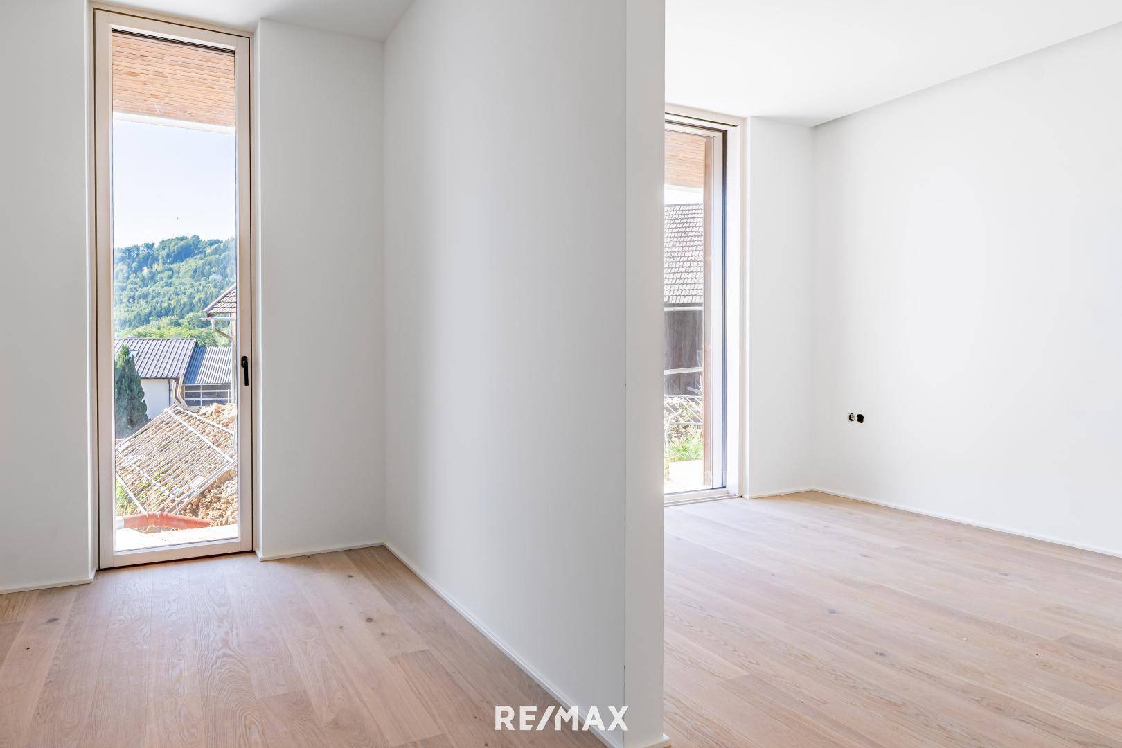 Lichtdurchfluteter Raum mit hellem Holzboden und hohen Fenstern, die viel Tageslicht hereinlassen.