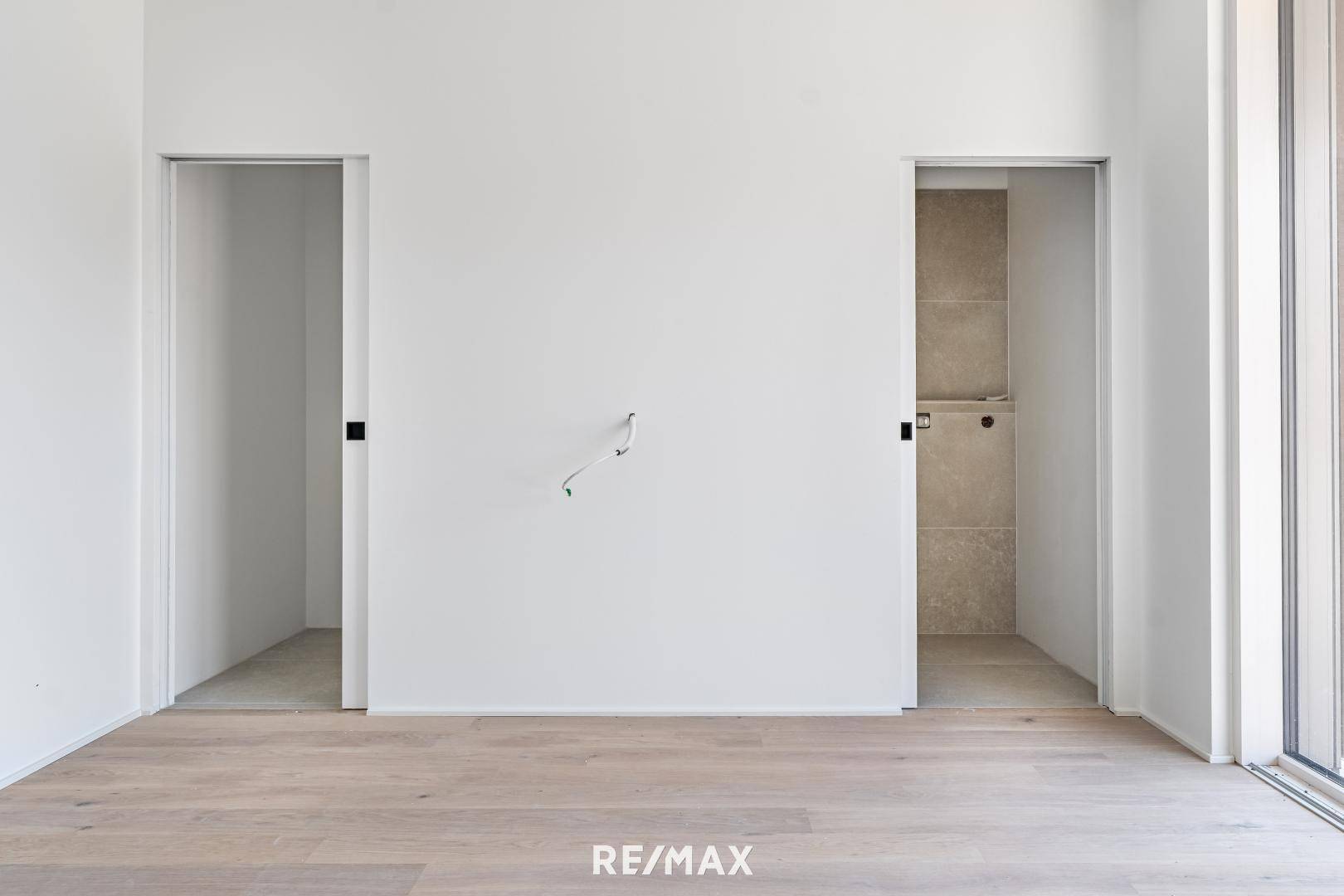 Leerer Raum mit Holzboden und zwei offenen Durchgängen, die zu weiteren Bereichen führen.