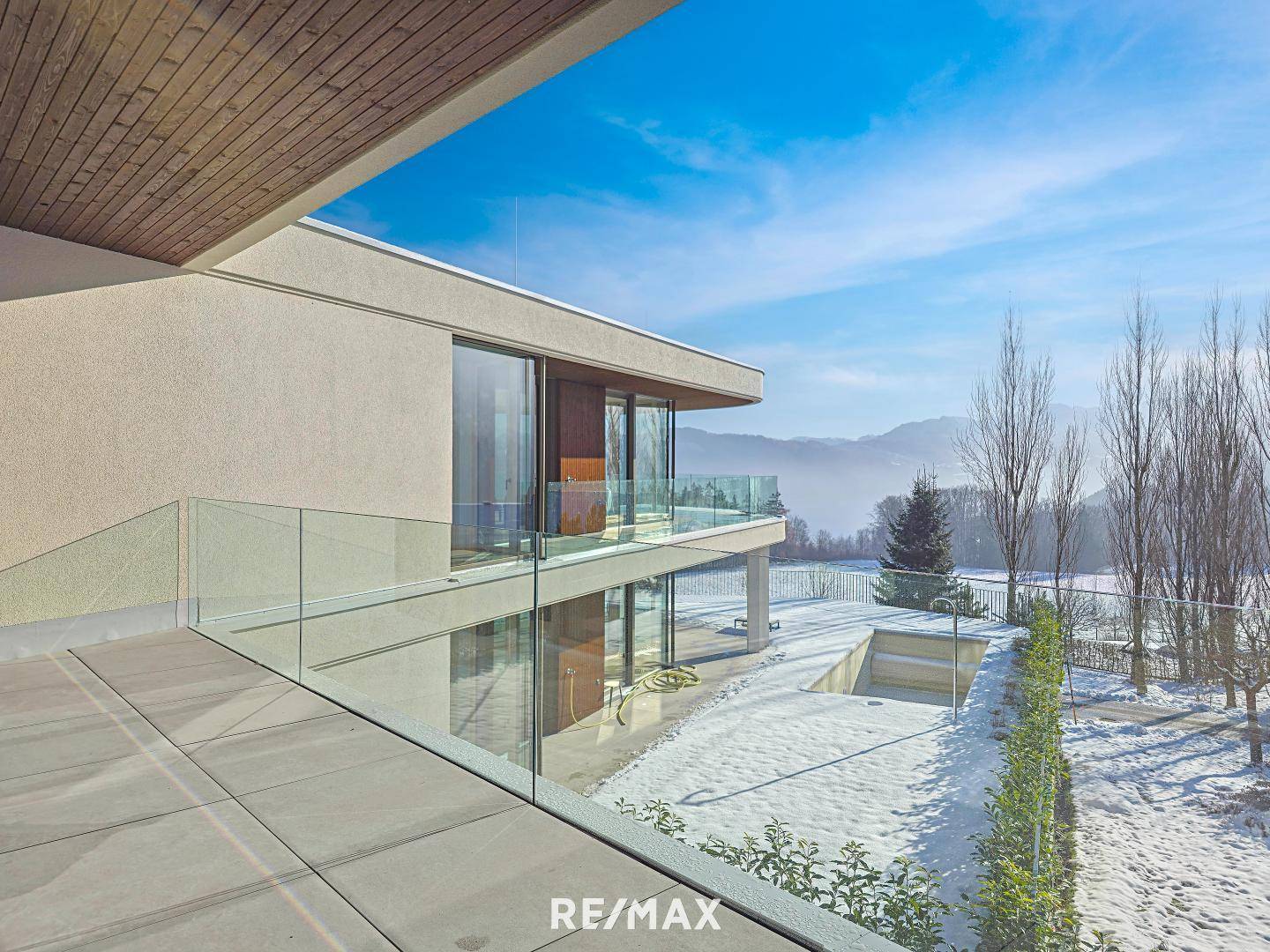 Geräumige Terrasse mit Glasgeländer und Panoramablick auf die winterliche Berglandschaft.