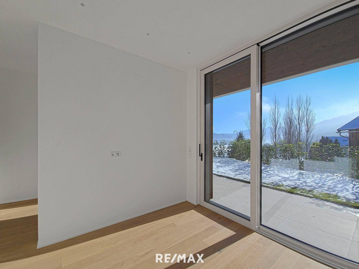 Heller Innenraum mit Holzboden und großer Schiebetür, die Zugang zur verschneiten Terrasse bietet.