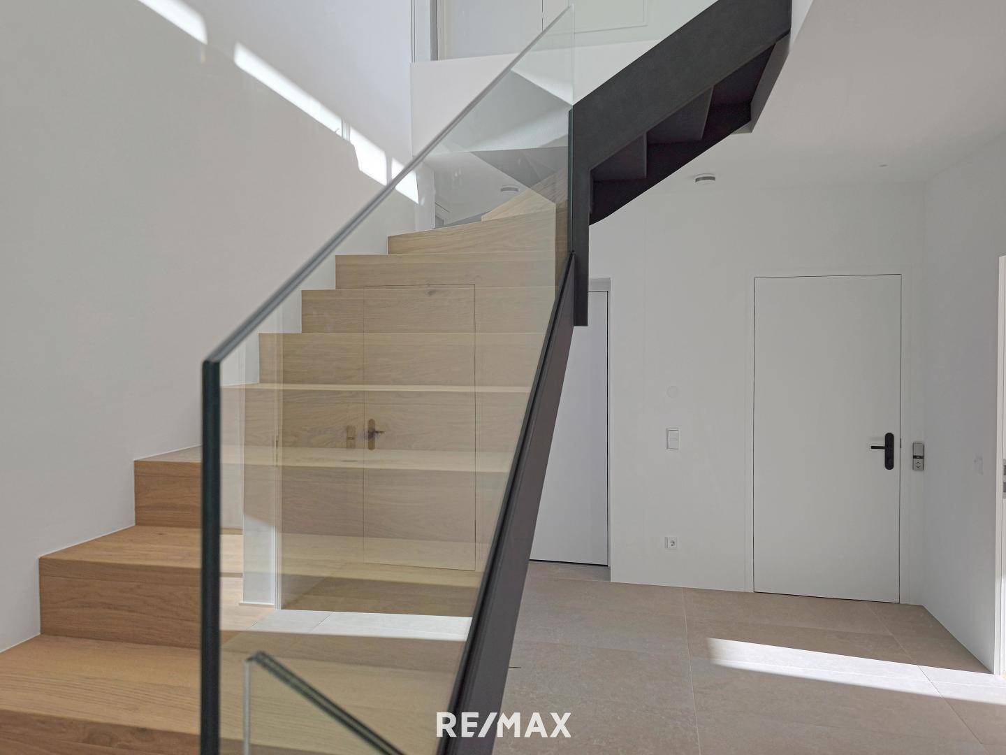 Elegante moderne Treppe mit Holzstufen und Glasgeländer, die die Etagen verbindet.