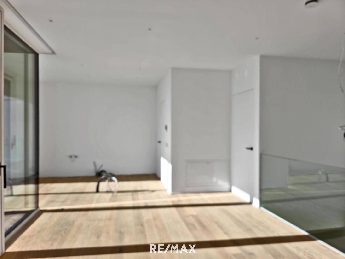 Geräumiger, heller Raum mit Holzboden und großen Fenstern, die viel Licht hereinlassen.