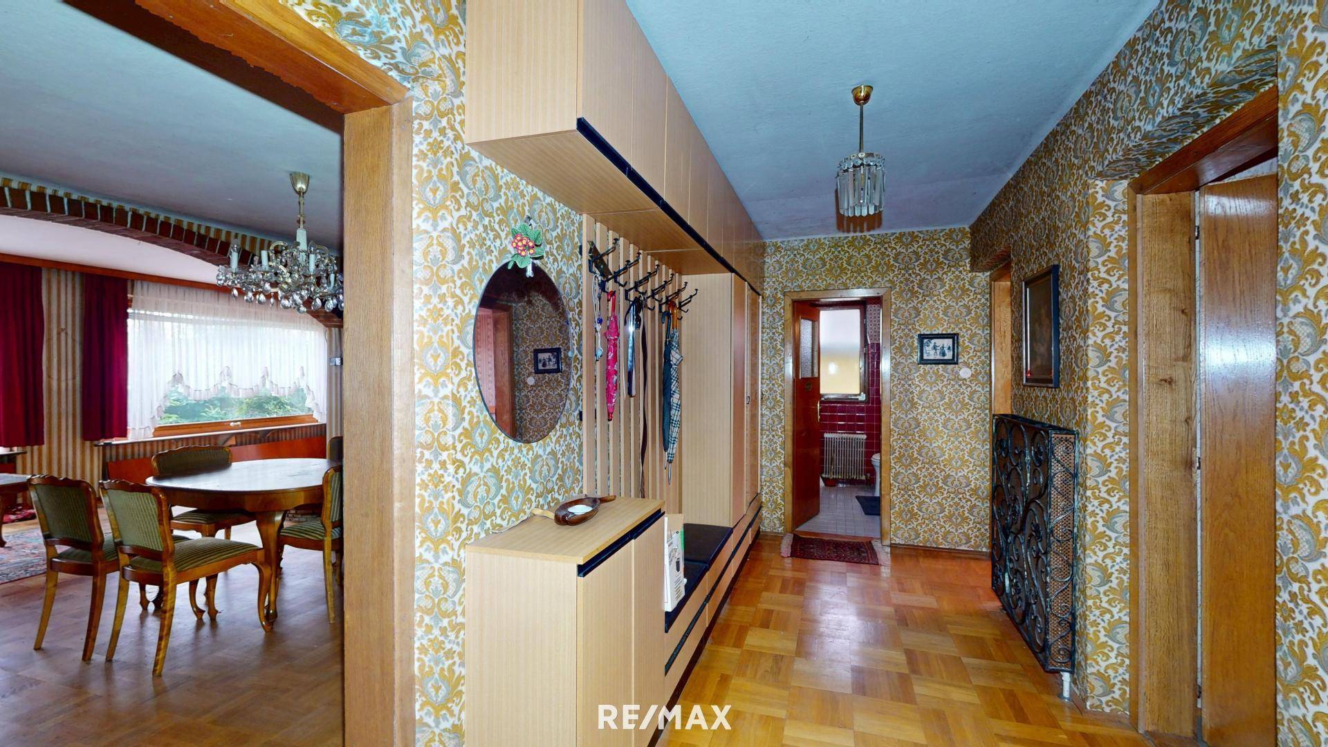 Langer Flur mit gemusterter Tapete, Holzparkett und Garderobe, der zu weiteren Räumen führt.