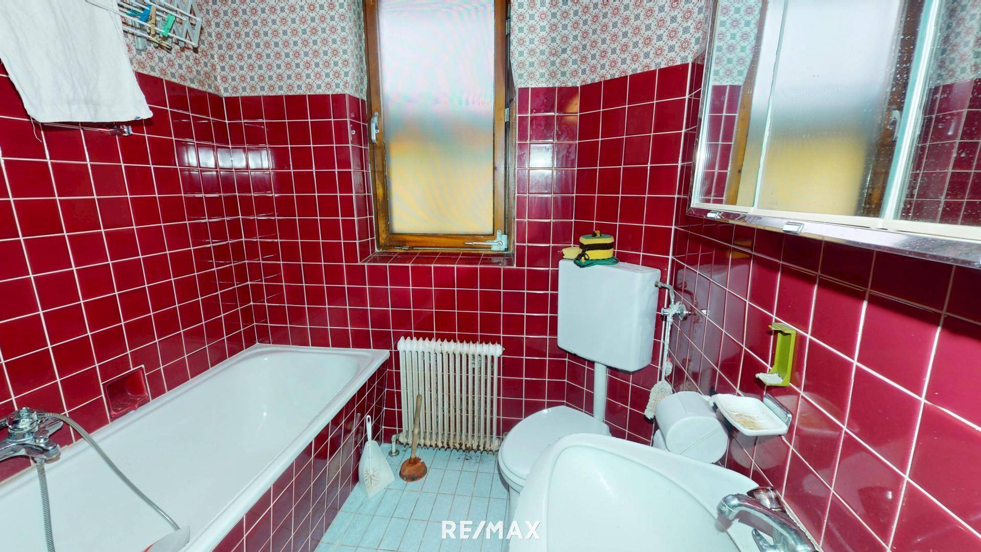 Badezimmer mit roten Fliesen, Badewanne, Toilette und Fenster für Tageslicht.