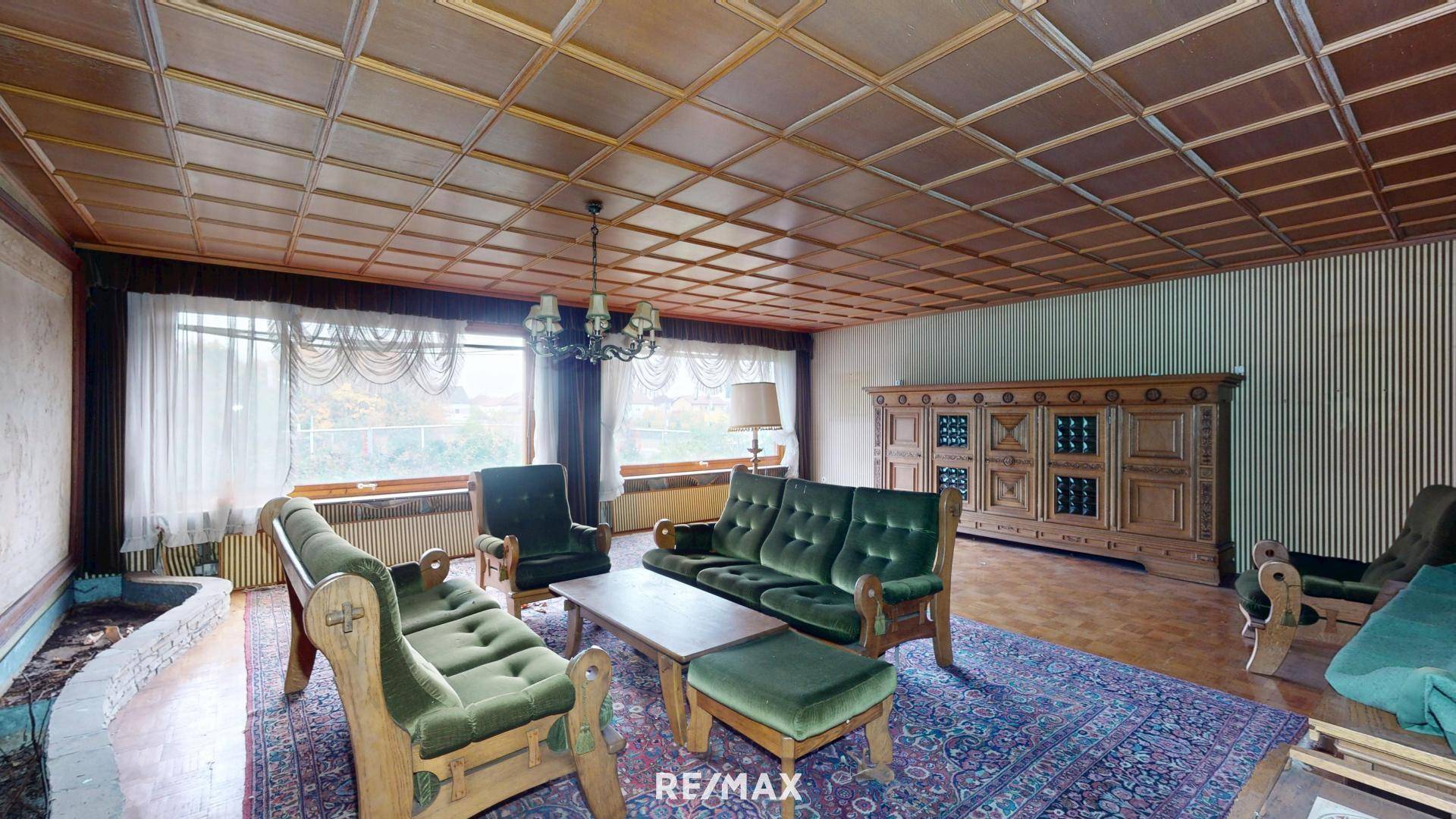 Geräumiges Wohnzimmer mit Holzkassettendecke, grünen Samtsofas und einem großen Teppich.