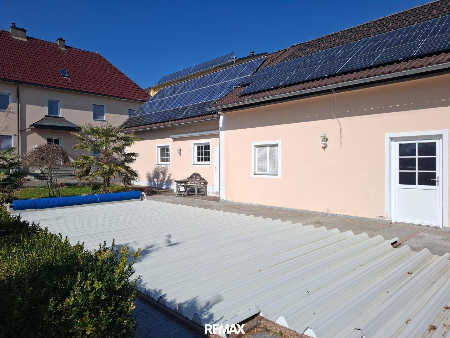 Rückseite des Hauses mit überdachtem Poolbereich und Photovoltaikanlage auf dem Dach.