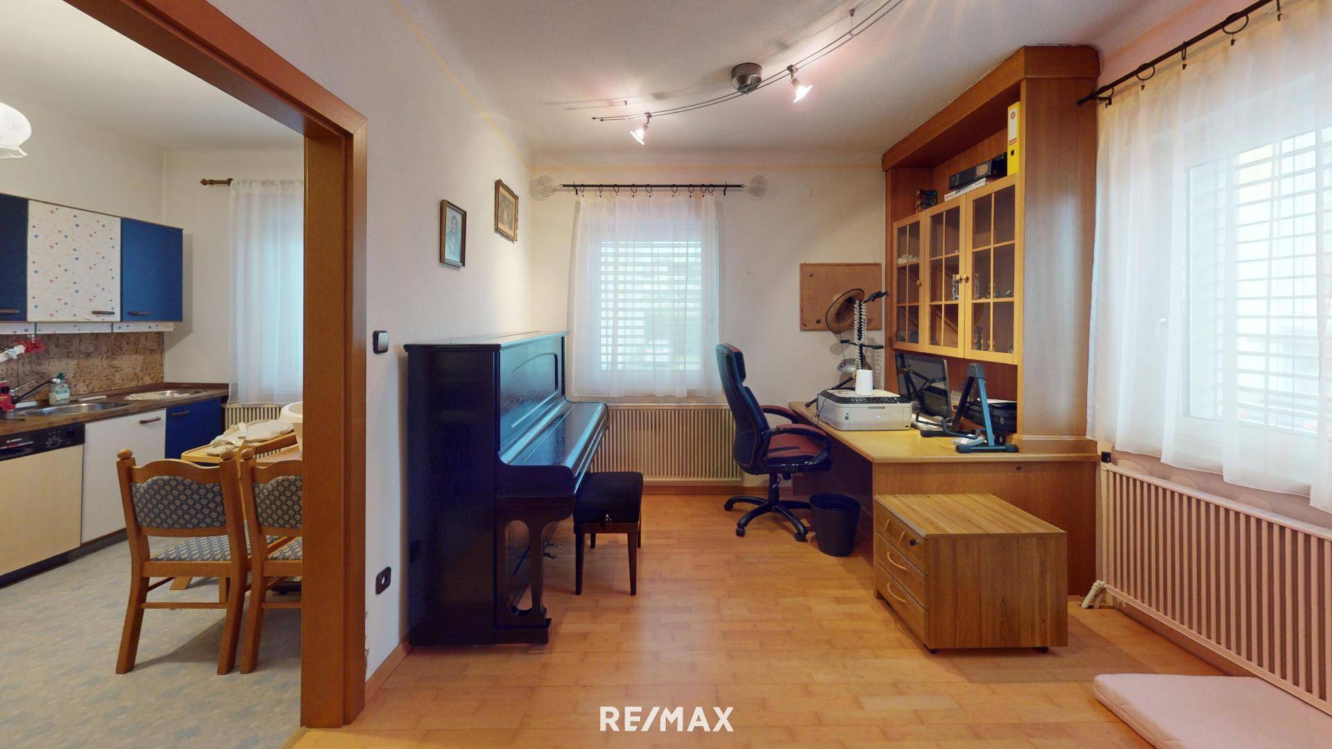 Helles Arbeitszimmer mit Holzmöbeln, Klavier und Blick in die Küche.