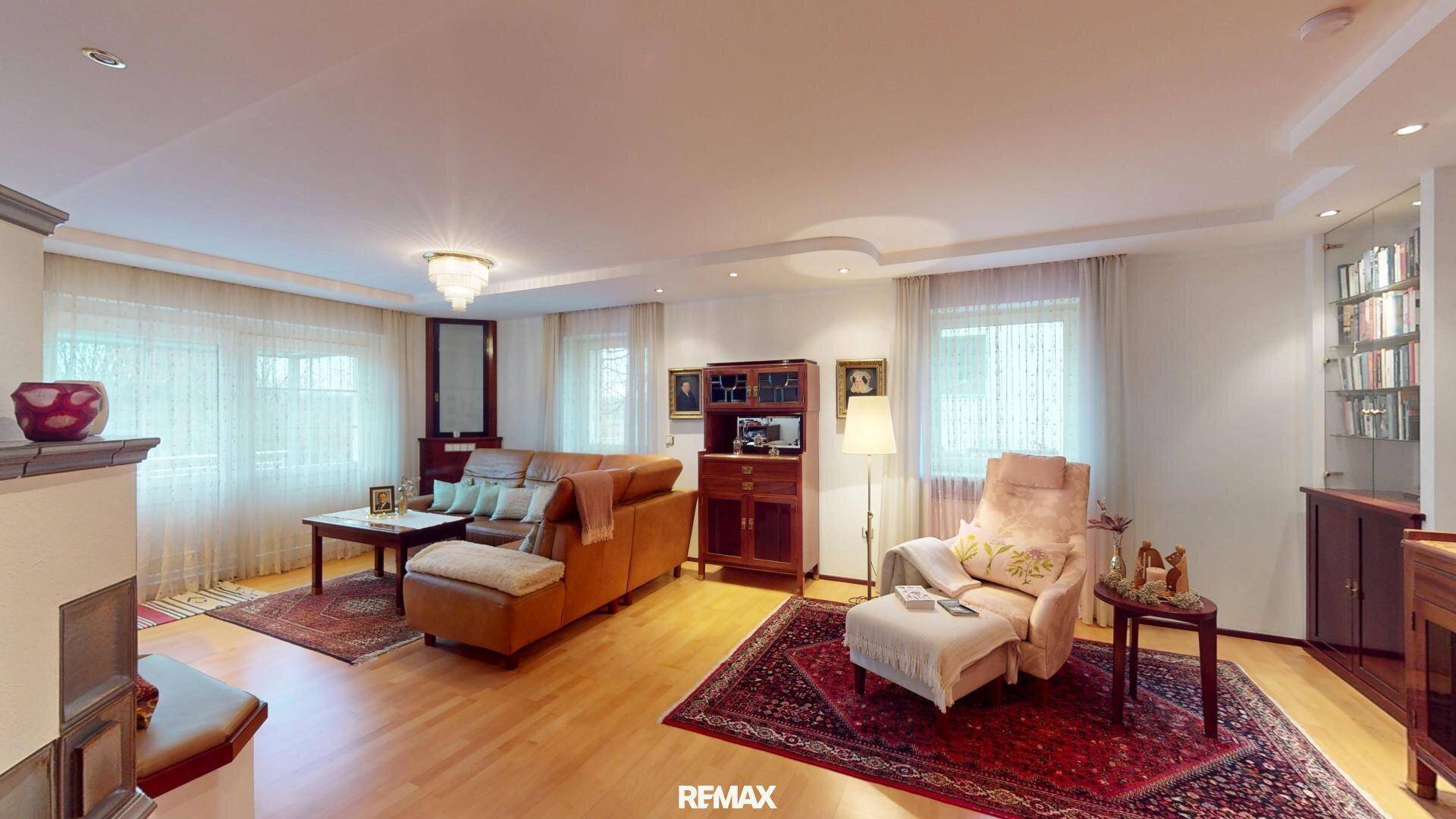 Geräumiges Wohnzimmer mit hellem Parkettboden, gemütlicher Sitzecke und Kachelofen.