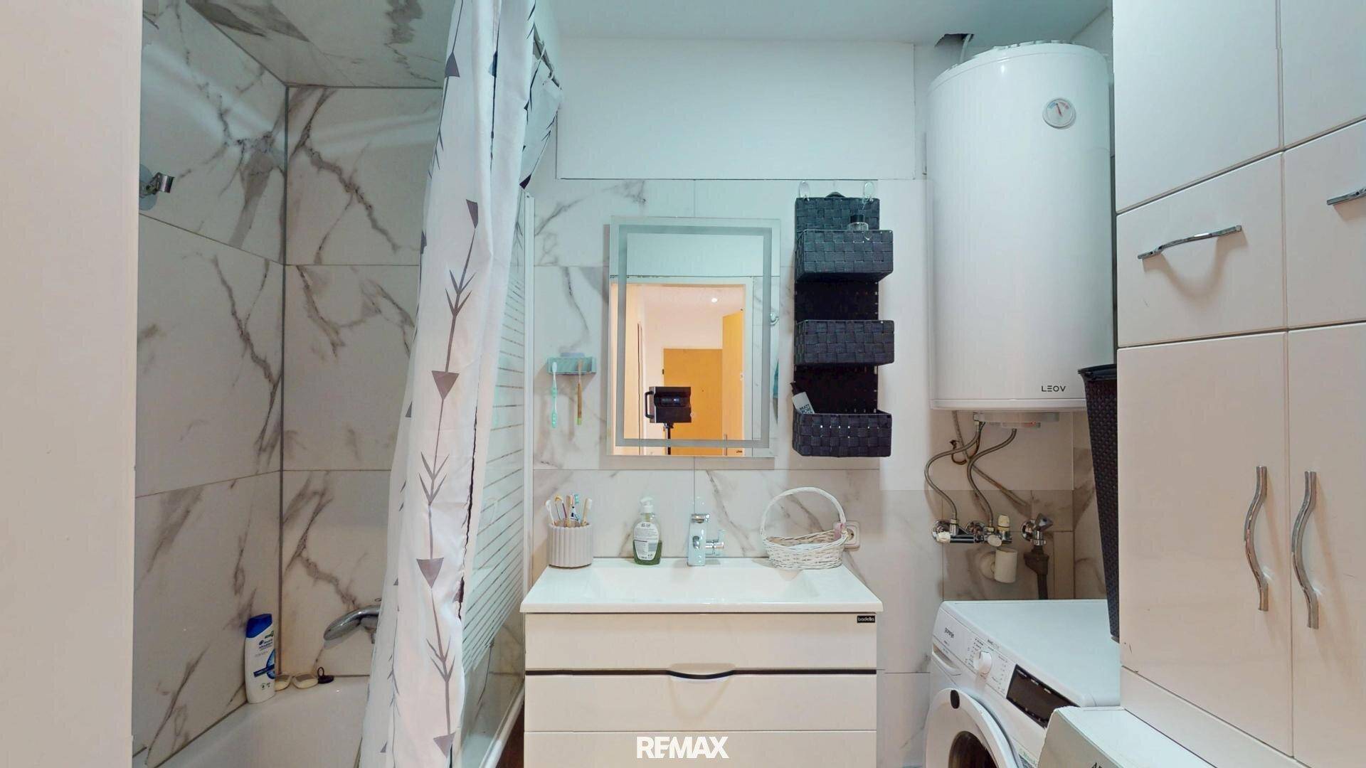 Modernes Badezimmer mit Badewanne, Waschmaschine und Marmoroptik-Fliesen.
