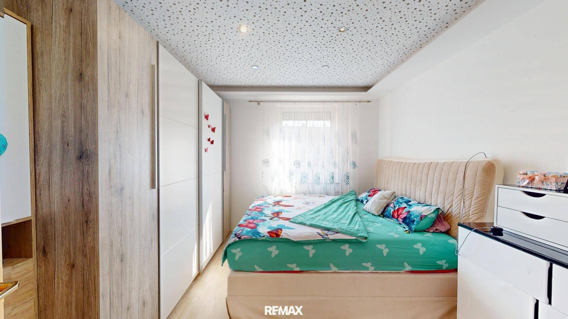 Helles Schlafzimmer mit Kleiderschrank, Bett und Fenster mit Tageslicht.