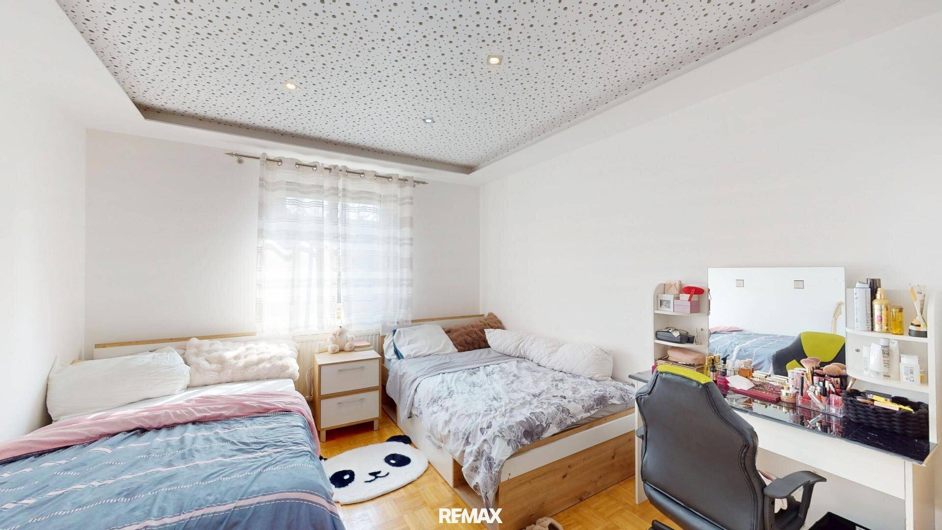 Kinderzimmer mit zwei Einzelbetten, Schreibtisch und Fenster mit Vorhängen.