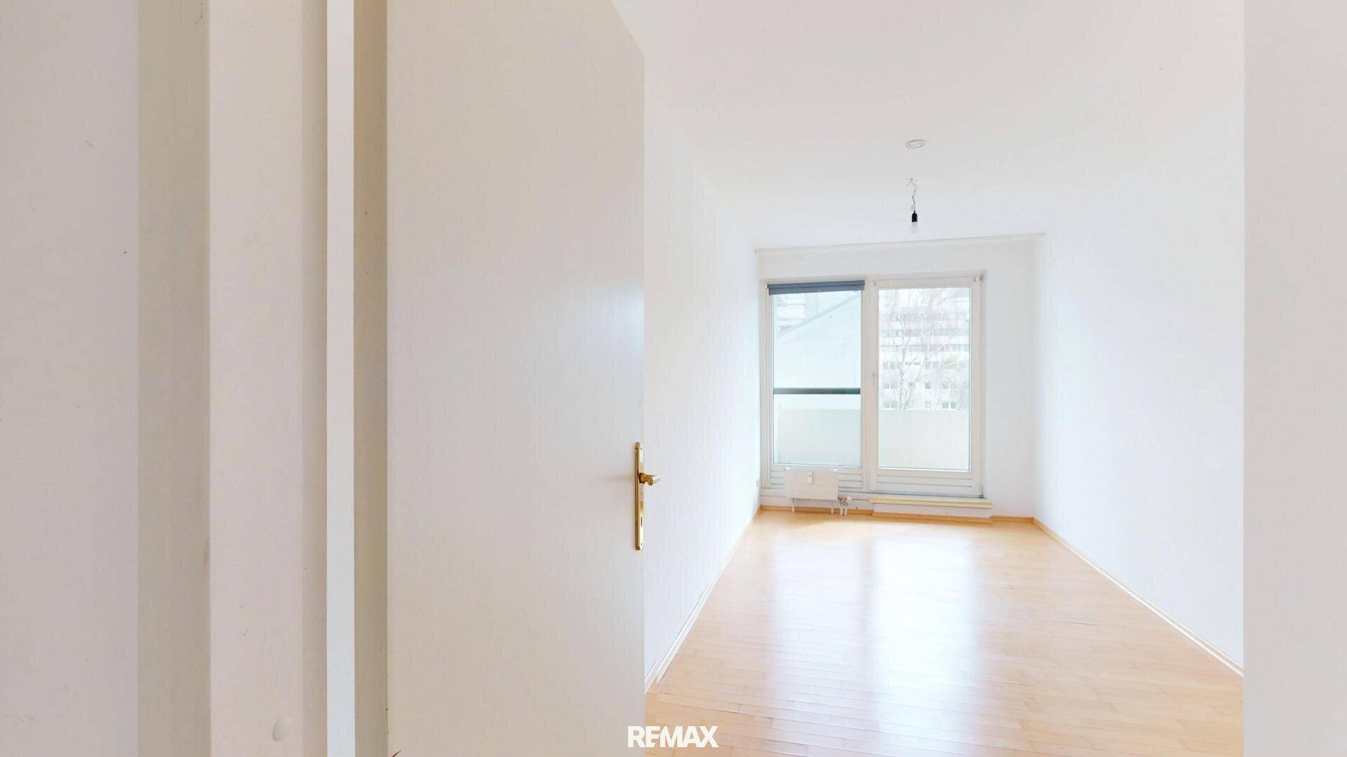 Leeres Wohnzimmer mit Parkettboden und viel Tageslicht durch die großen Fenster.