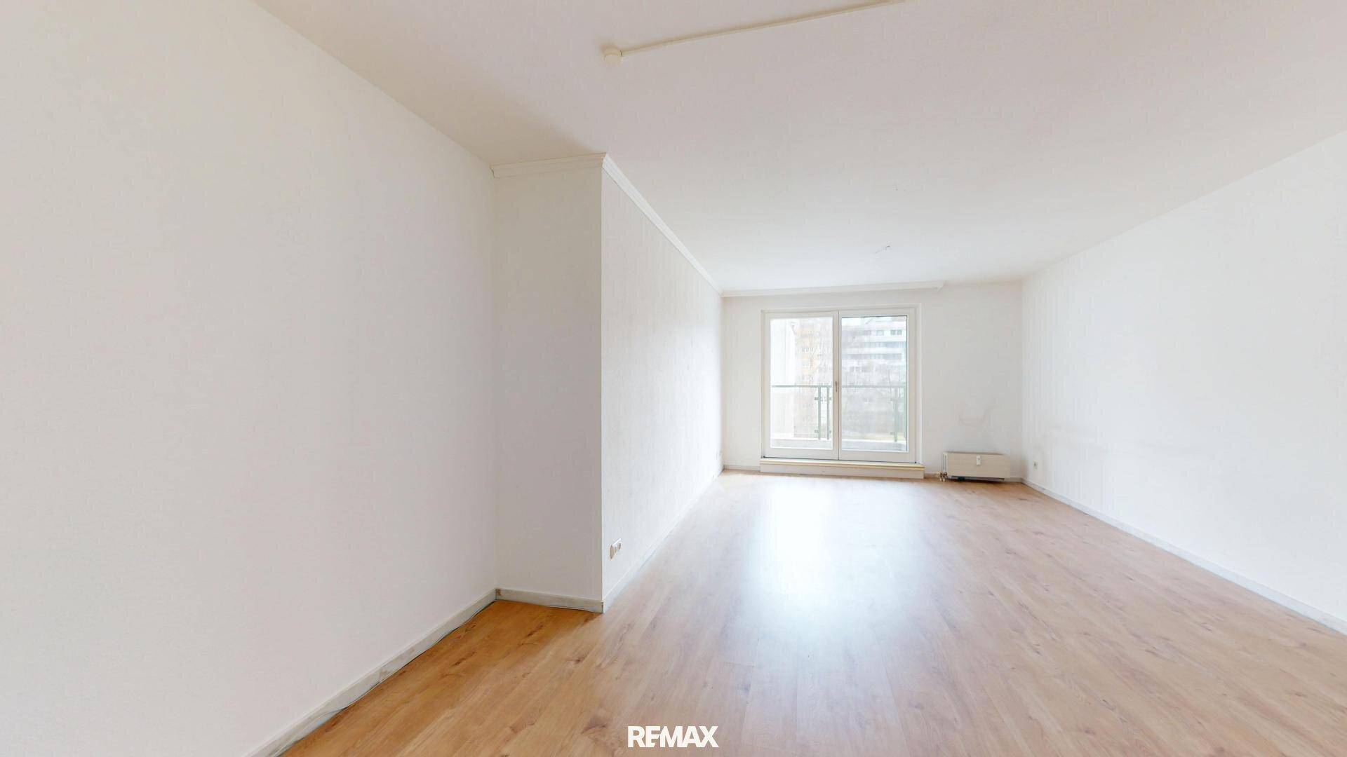 Geräumiges, leeres Wohnzimmer mit hellem Parkettboden und Zugang zu einem französischen Balkon.