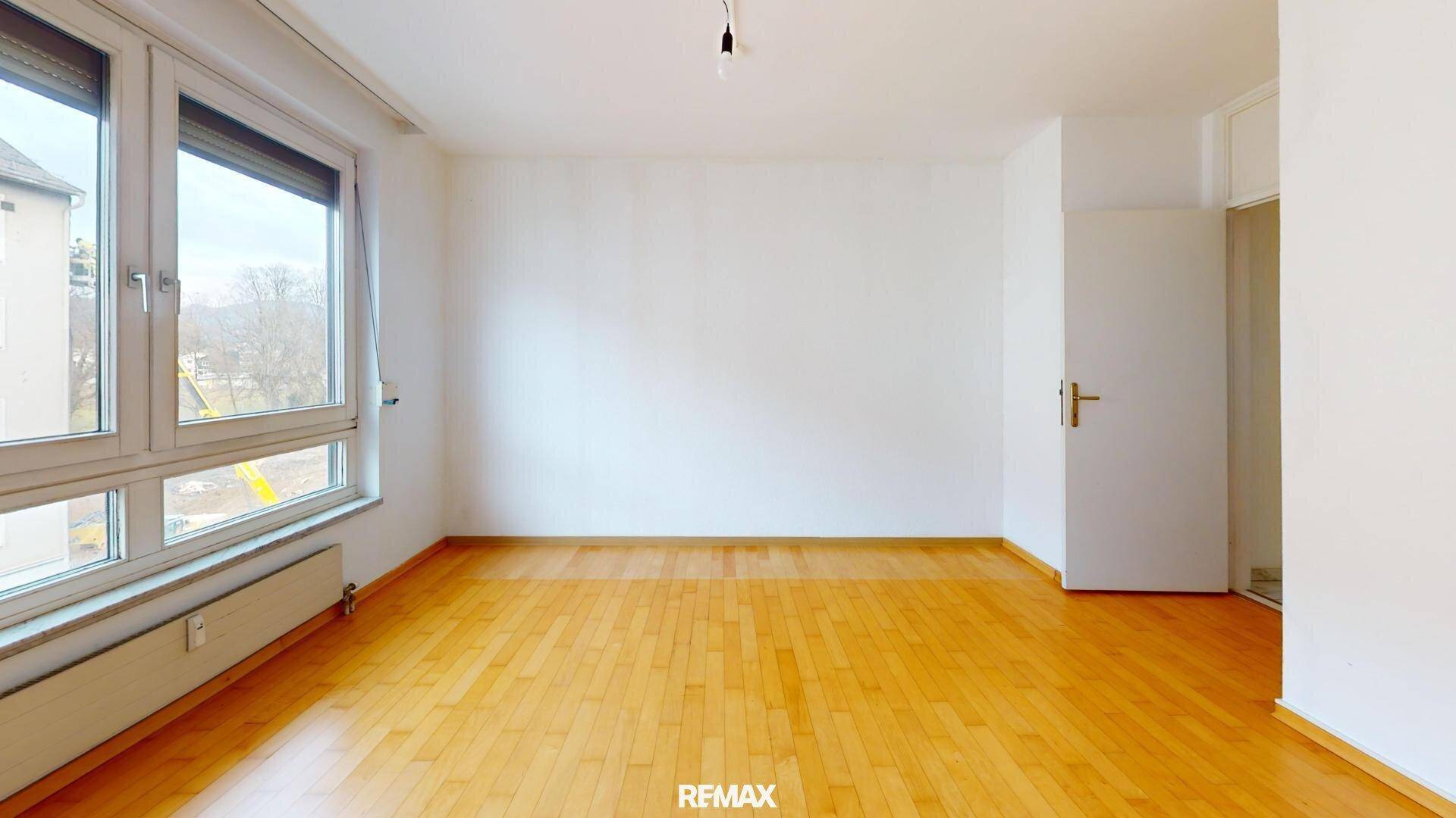 Helles Wohnzimmer mit großen Fenstern, Parkettboden und Blick ins Grüne.