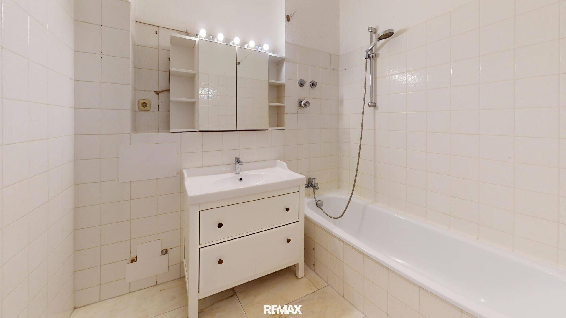 Badezimmer mit Badewanne, Waschbecken und weißen Fliesen, bereit zur Modernisierung.