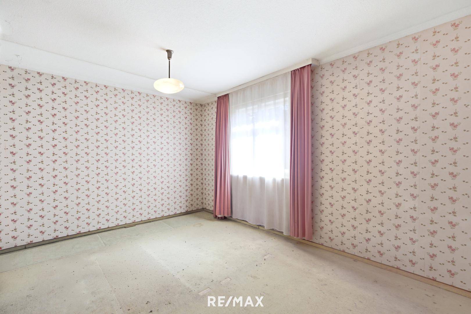 Schlafzimmer mit floraler Tapete, einem Fenster und einfacher Deckenbeleuchtung.