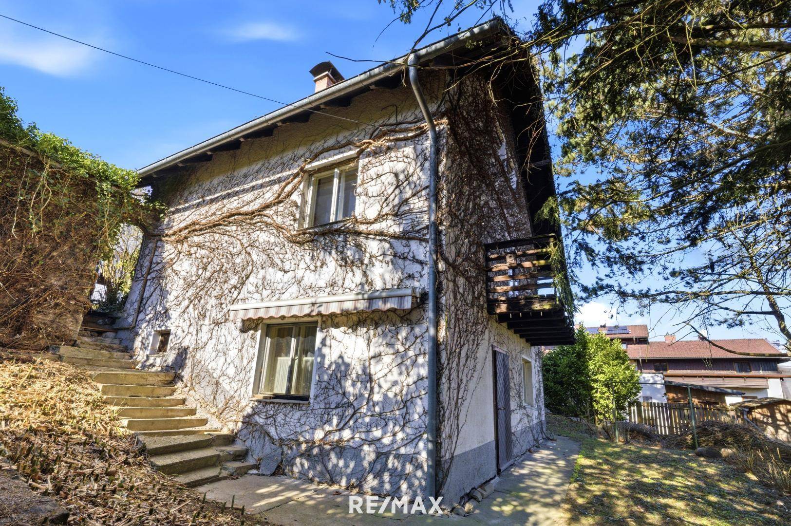 Rückansicht des Hauses mit Außentreppe, kleinem Balkon und bewachsener Fassade.