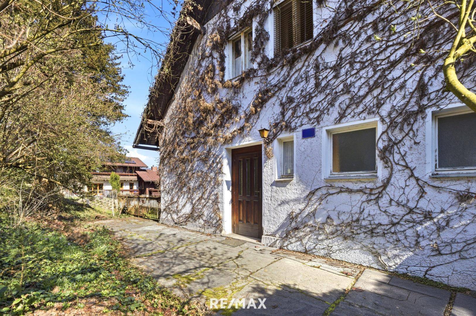 Seitlicher Eingangsbereich des Hauses mit Holztür und bewachsener Fassade.
