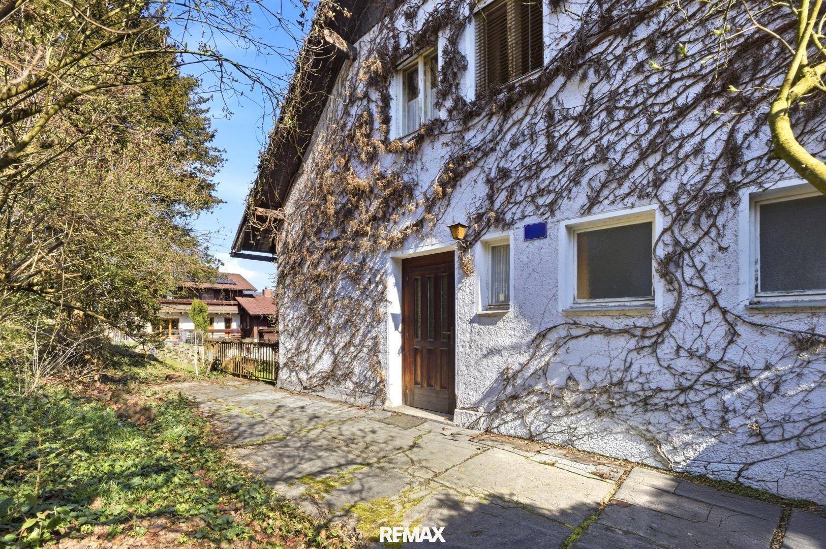 Eingangsbereich eines älteren Hauses mit bewachsener Fassade und Holztür.