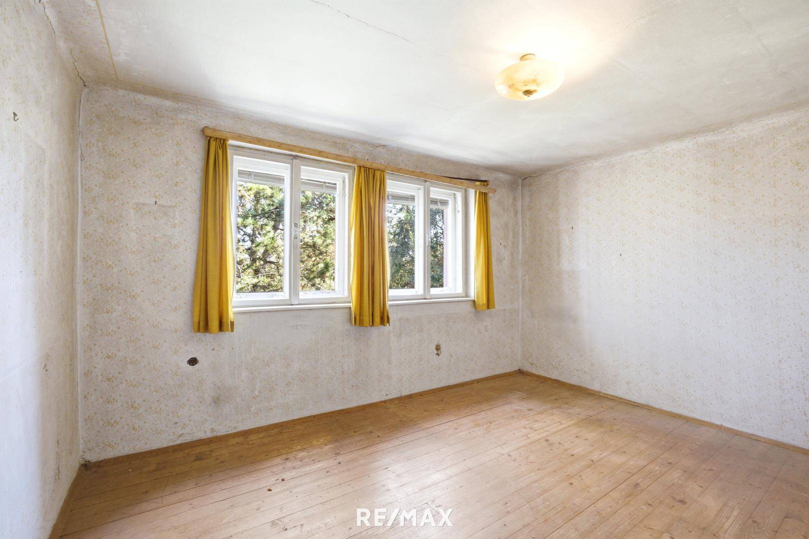 Helles Schlafzimmer mit Holzdielenboden und Blick ins Grüne durch große Fenster.