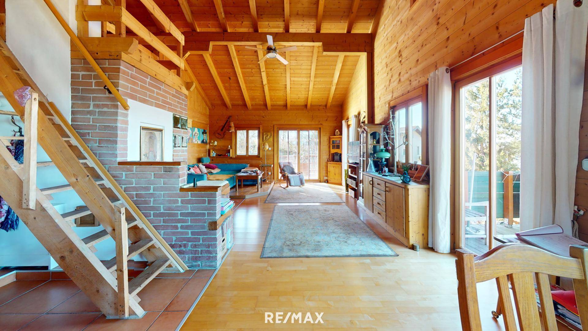 Geräumiges Wohnzimmer mit Holzvertäfelung, offener Treppe und viel natürlichem Licht.
