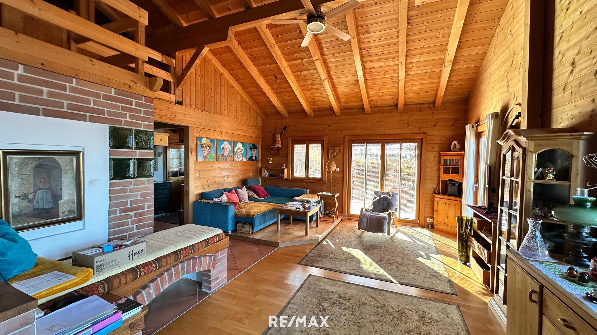 Rustikales Wohnzimmer mit Holzwänden, hohen Decken, sichtbaren Balken und einem gemütlichen Kamin.