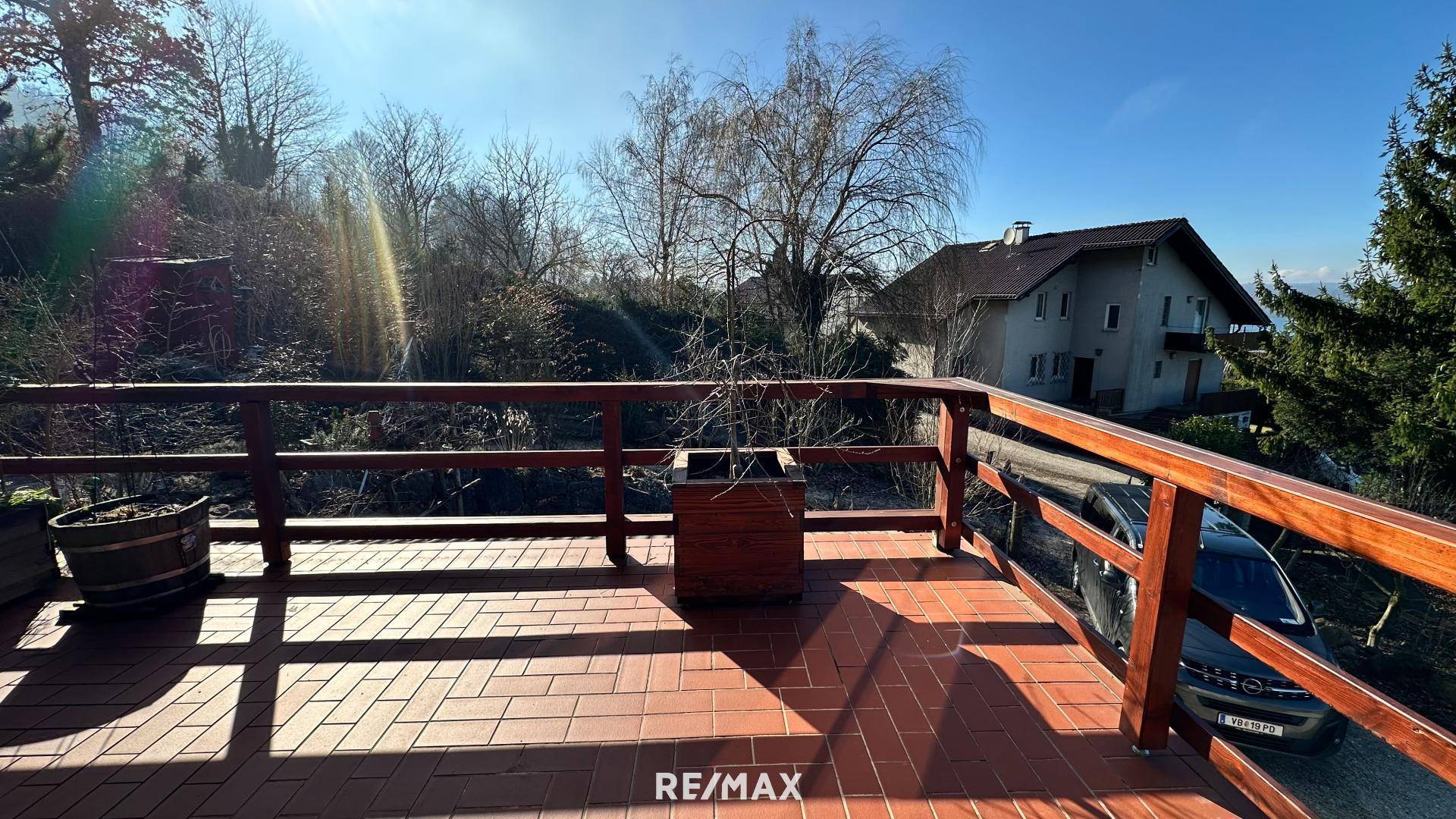Sonnige Terrasse mit Terrakotta-Fliesenboden und Holzgeländer, umgeben von Bäumen.