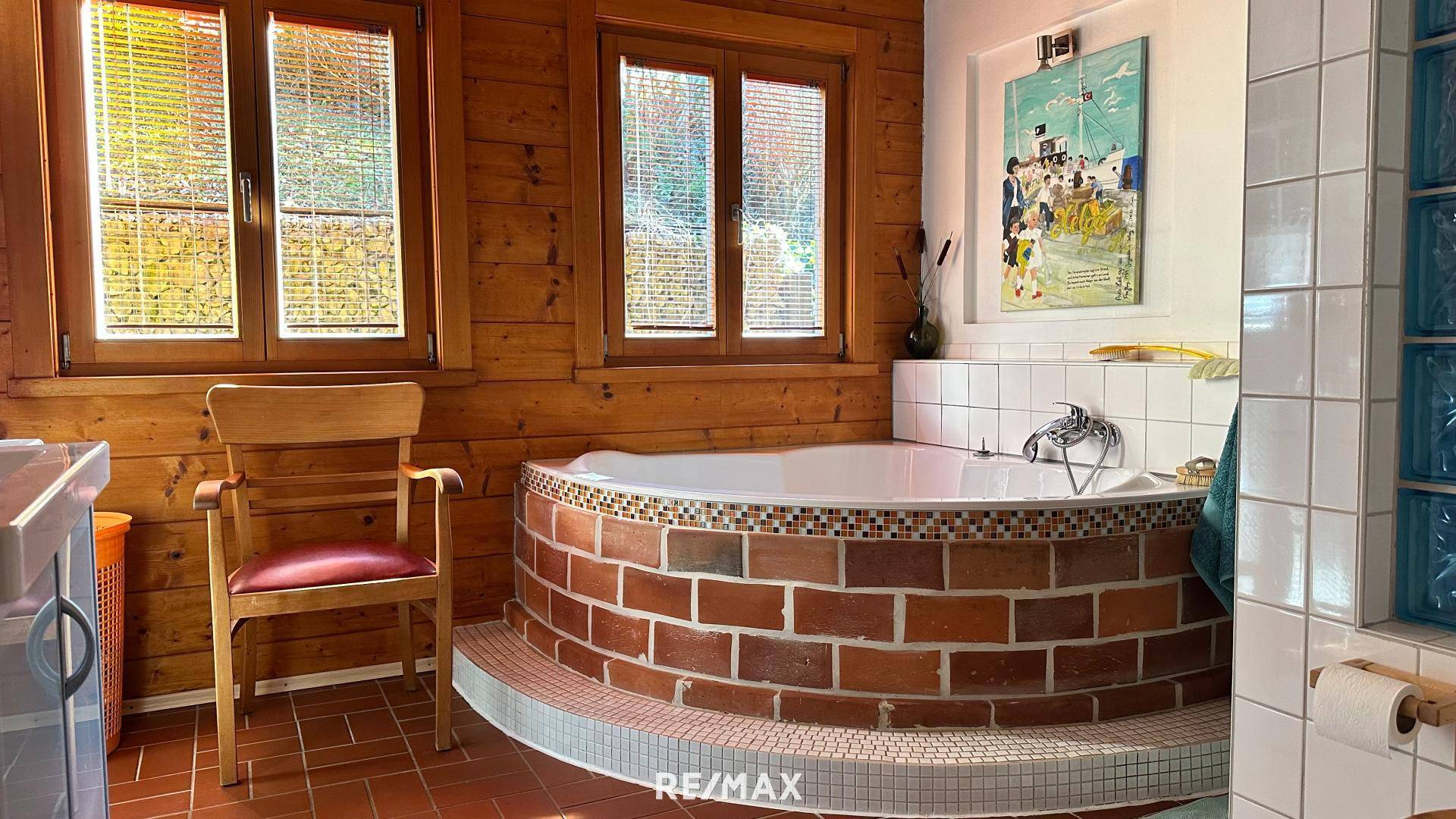 Badezimmer mit einer runden Badewanne auf gemauertem Sockel und Holzvertäfelung an den Wänden.