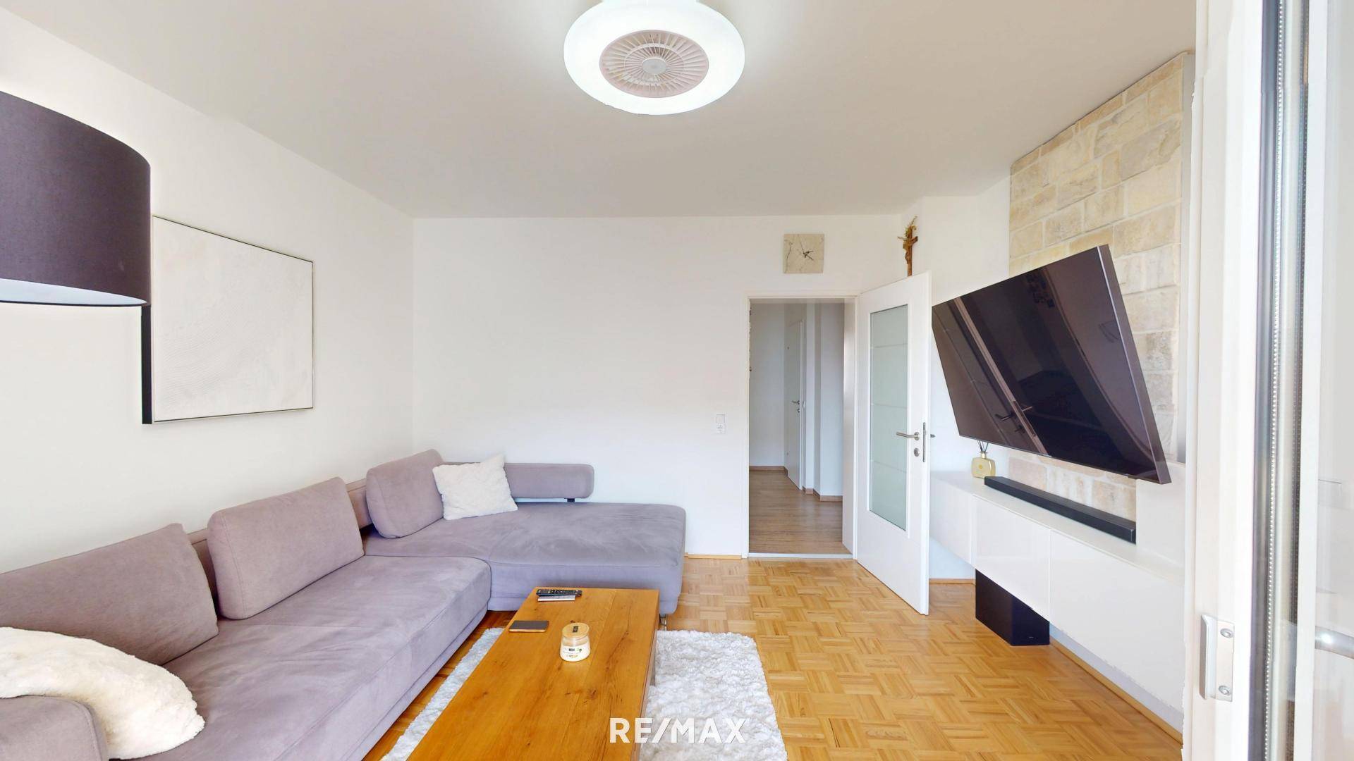 Helles Wohnzimmer mit Ecksofa, Fernseher und Zugang zum Außenbereich.